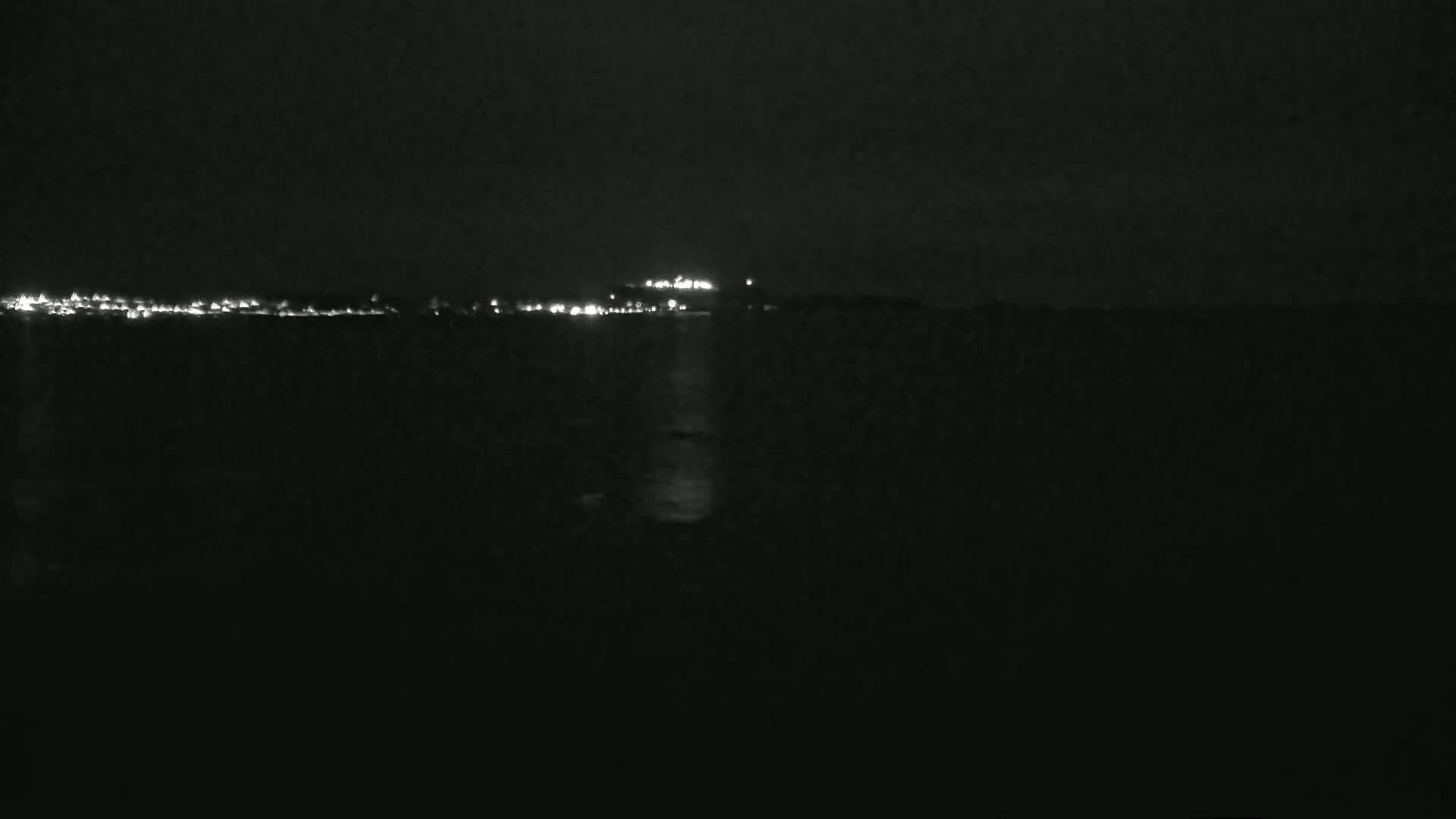 A dark, nighttime view of a body of water reflecting the lights of a distant city on the horizon.