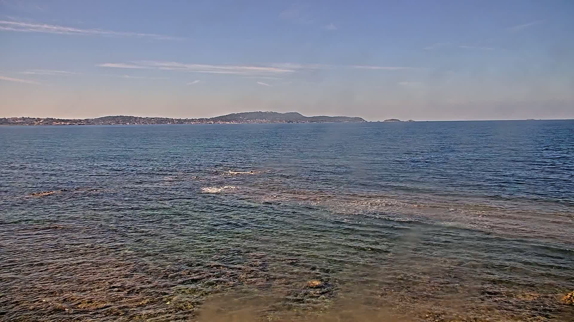A calm sea with a distant shoreline under a mostly clear sky.