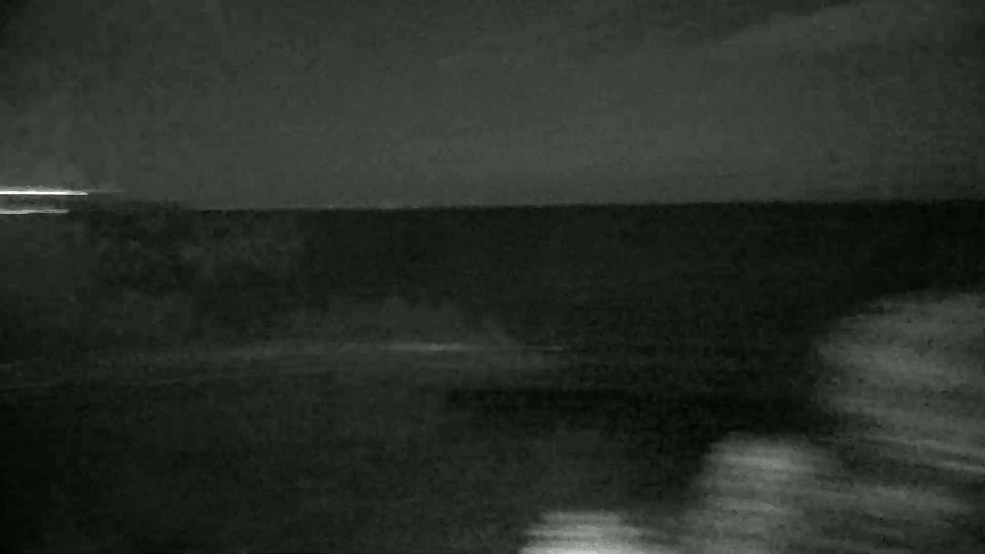 A dark, nighttime view of a body of water under a mostly clear sky shows a faint horizon line.