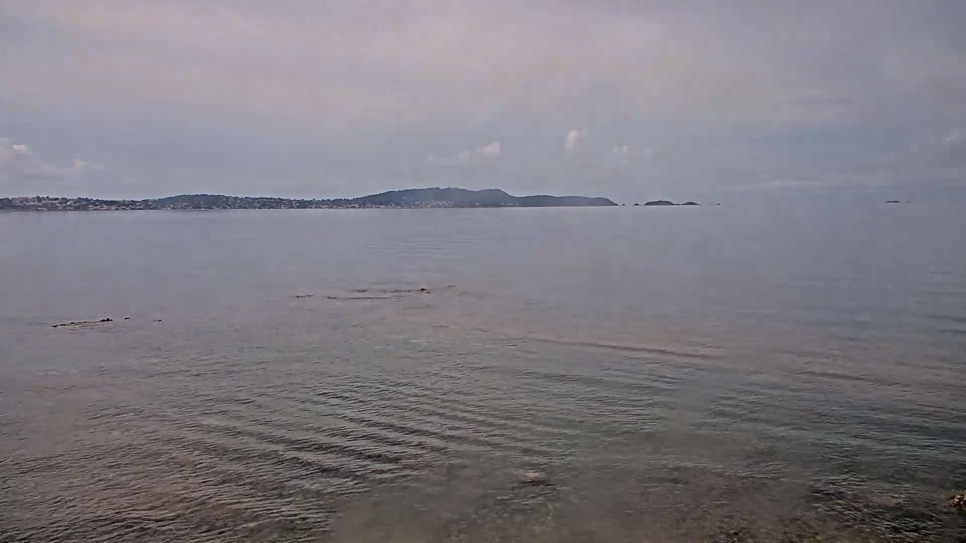 Calm, overcast water shows a distant shoreline with low hills under a cloudy sky.