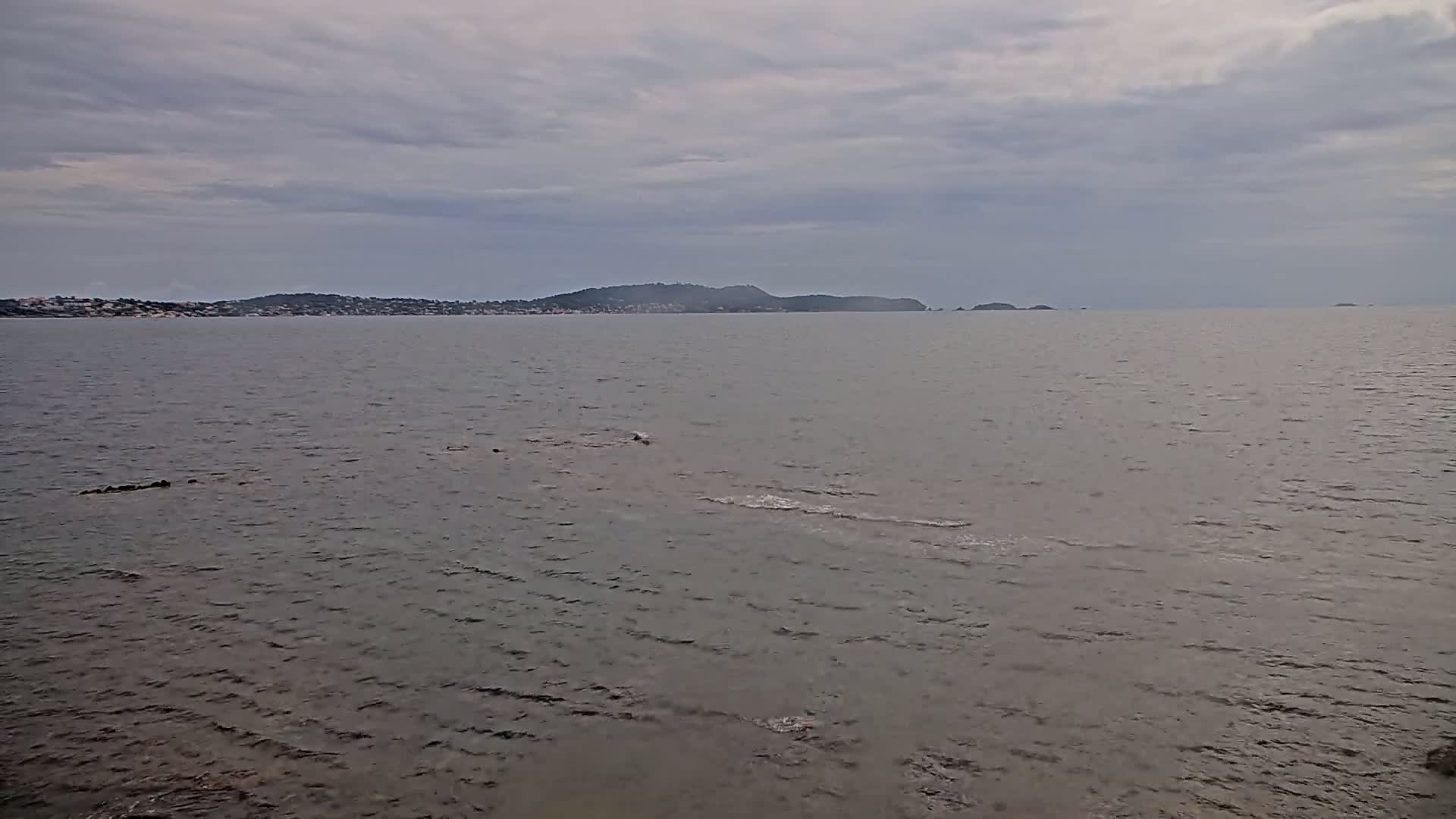 A calm, gray sea stretches toward a distant, low-lying coastline under a cloudy sky.