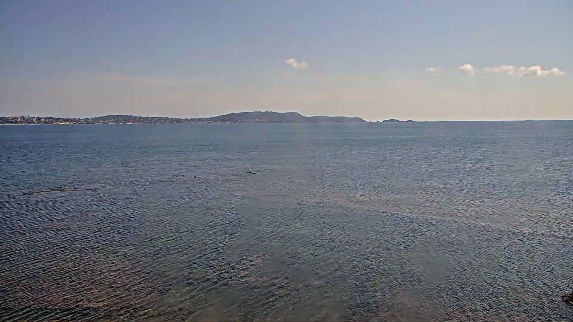 A calm, clear day shows a body of water with a distant shoreline and small islands under a mostly clear sky.