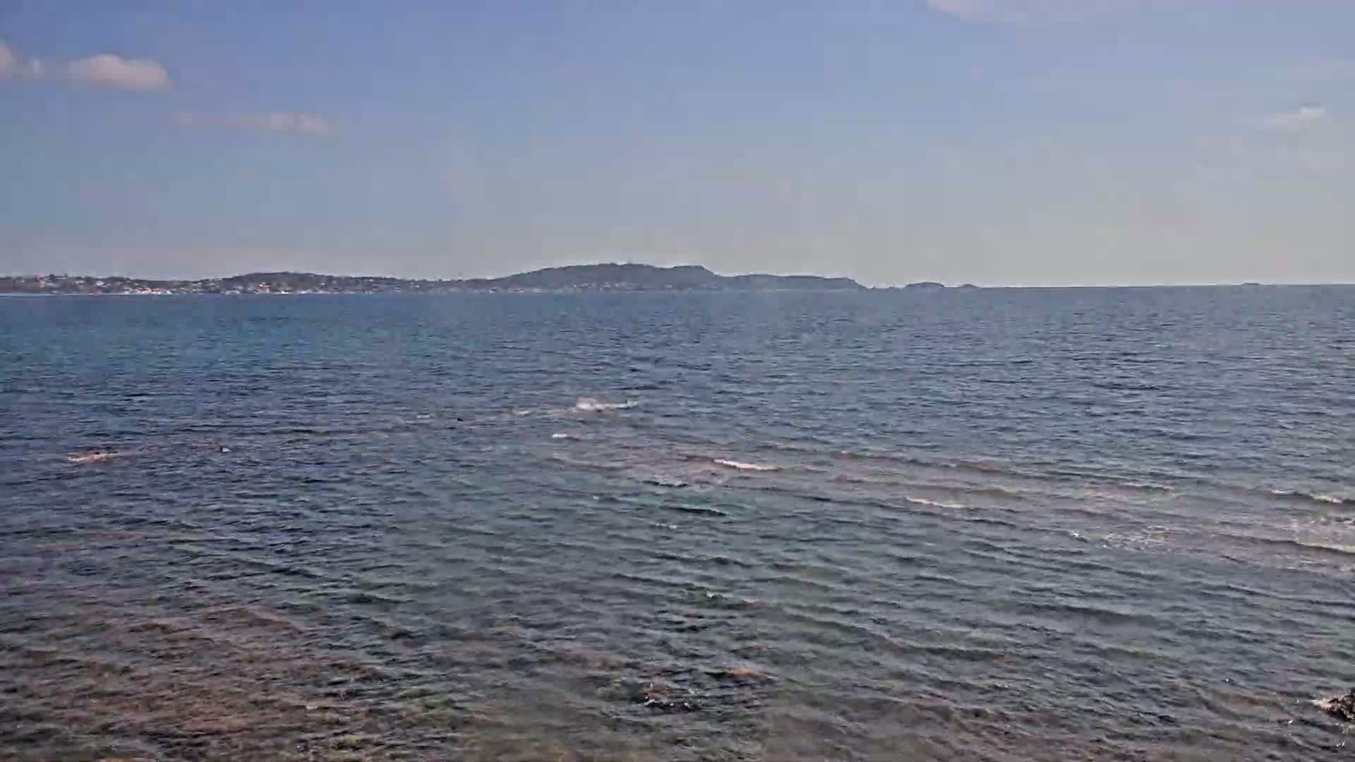 A calm, blue sea stretches to a distant shoreline under a clear, bright sky.