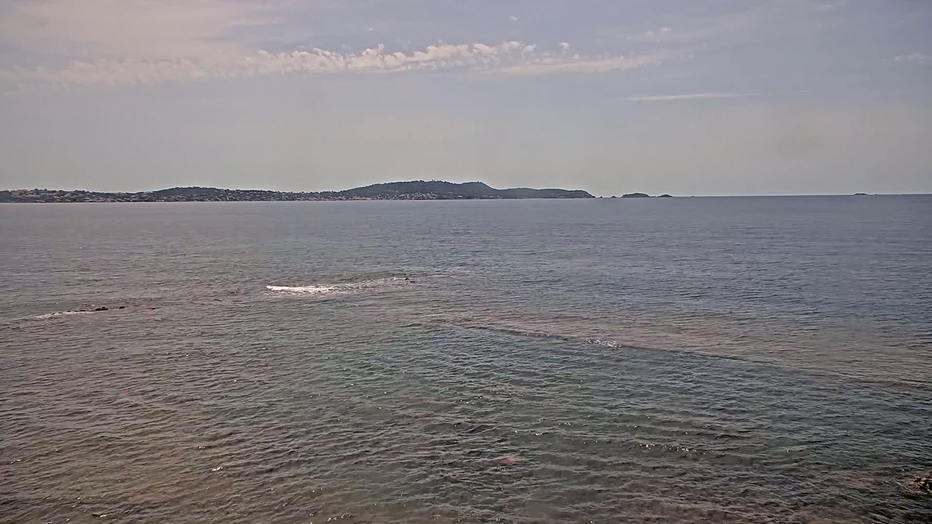 A calm sea with a distant, low-lying landmass under a partly cloudy sky.