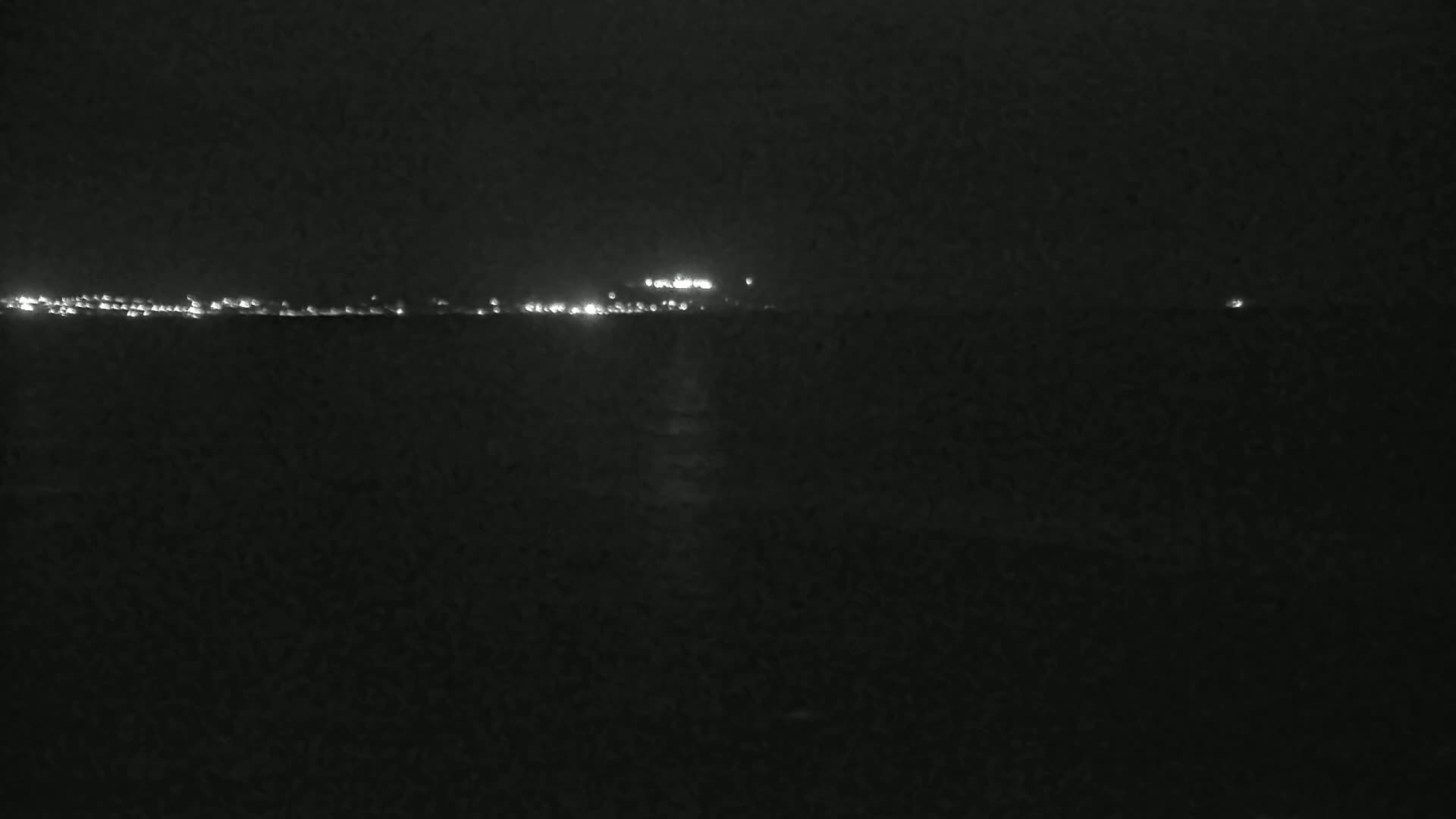 A dark, nighttime view shows a distant line of city lights across a dark body of water.