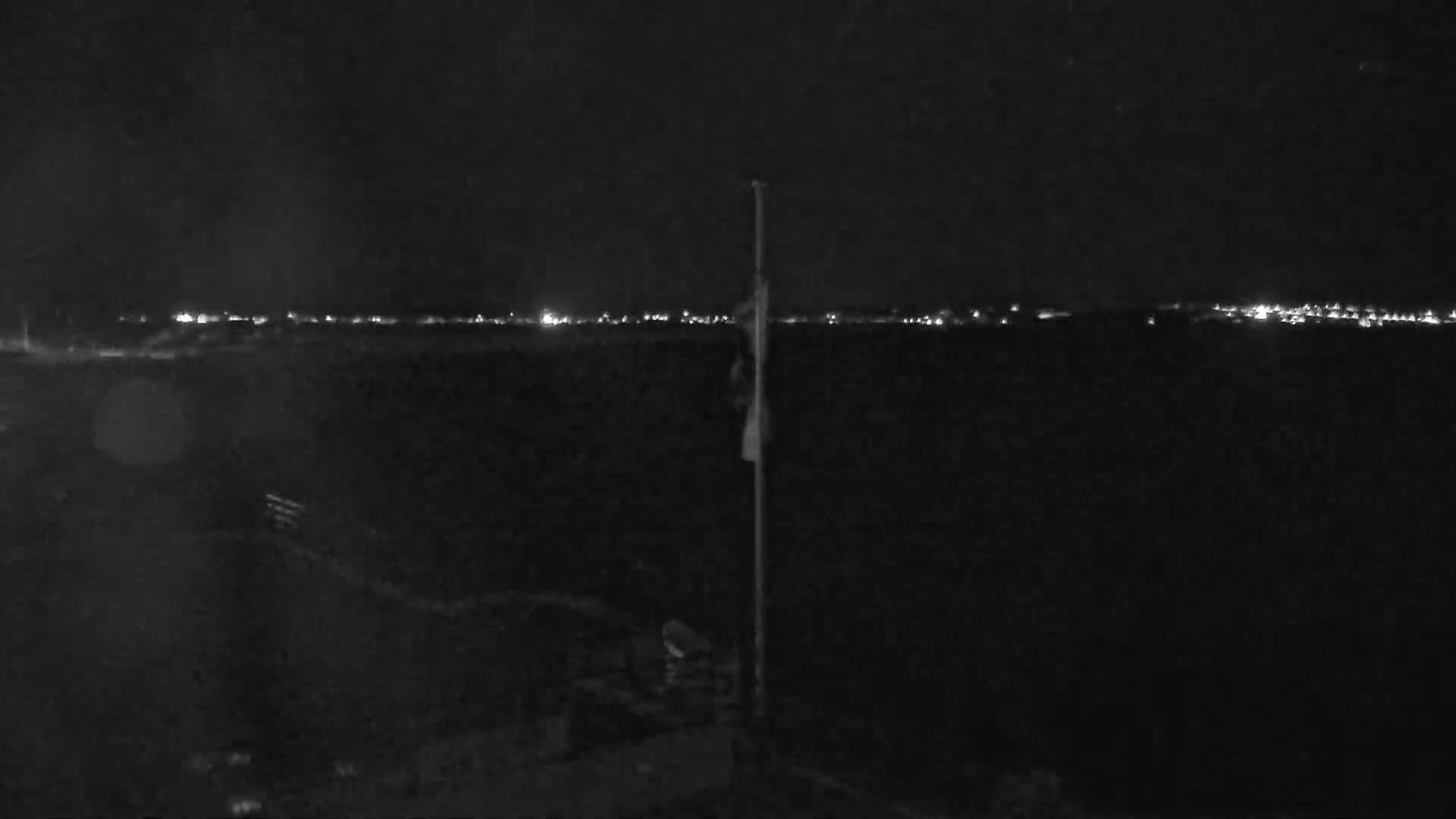 A nighttime, low-light view shows a flagpole and a distant line of city lights.
