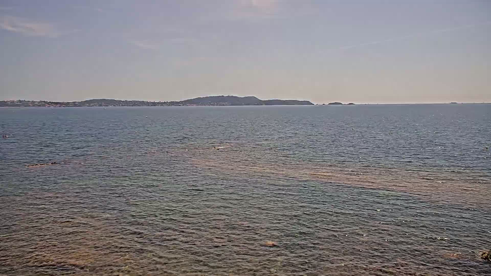 A calm, clear day shows a view of a body of water with a distant shoreline and islands under a pale blue sky.
