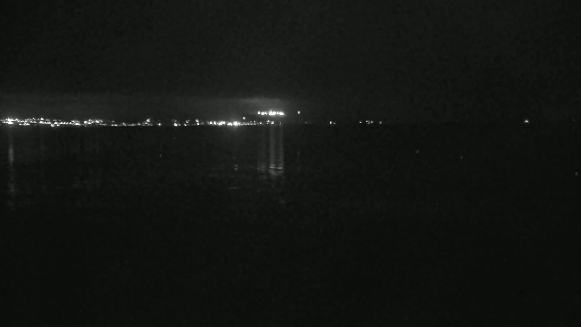 A dark, nighttime scene shows a distant city skyline illuminated by lights across a body of water.