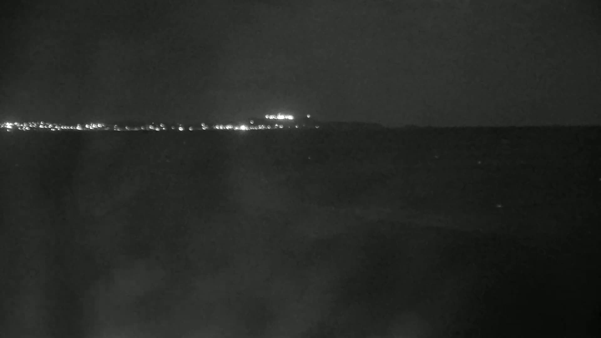 A dark, nighttime scene shows a distant line of lights on a hill or ridge.