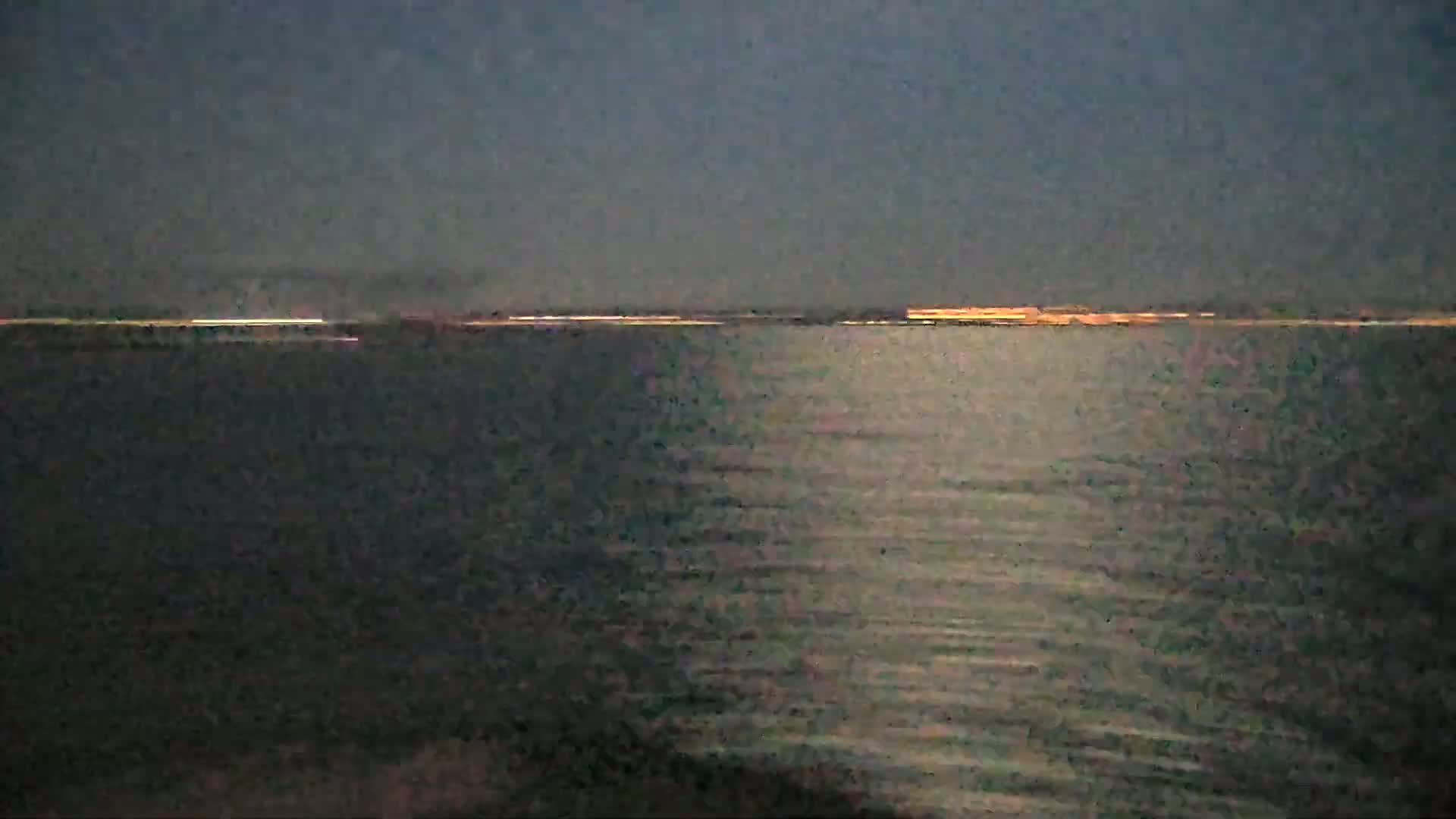 A dark body of water reflects a faint orange glow on the horizon under a dusky sky.