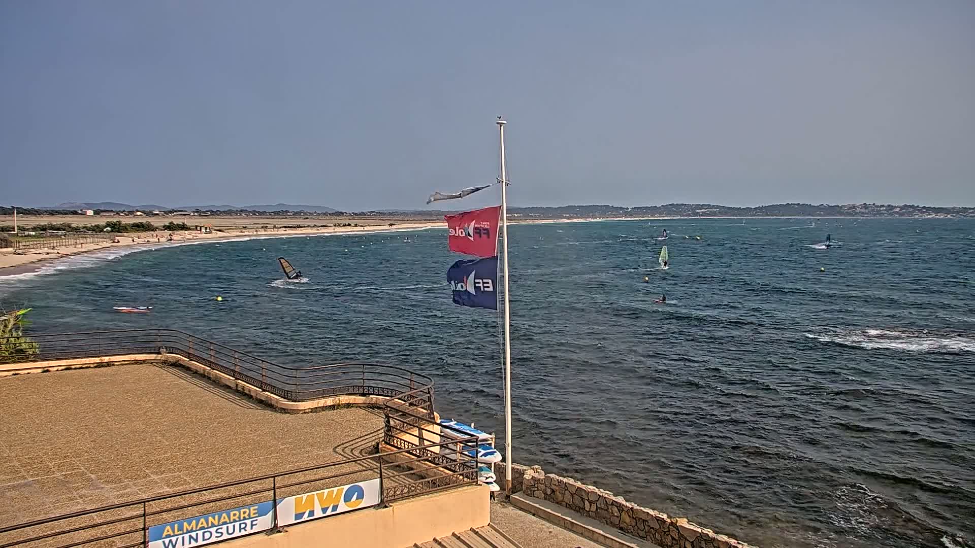 A sandy beach with several windsurfers in the ocean on a sunny day.