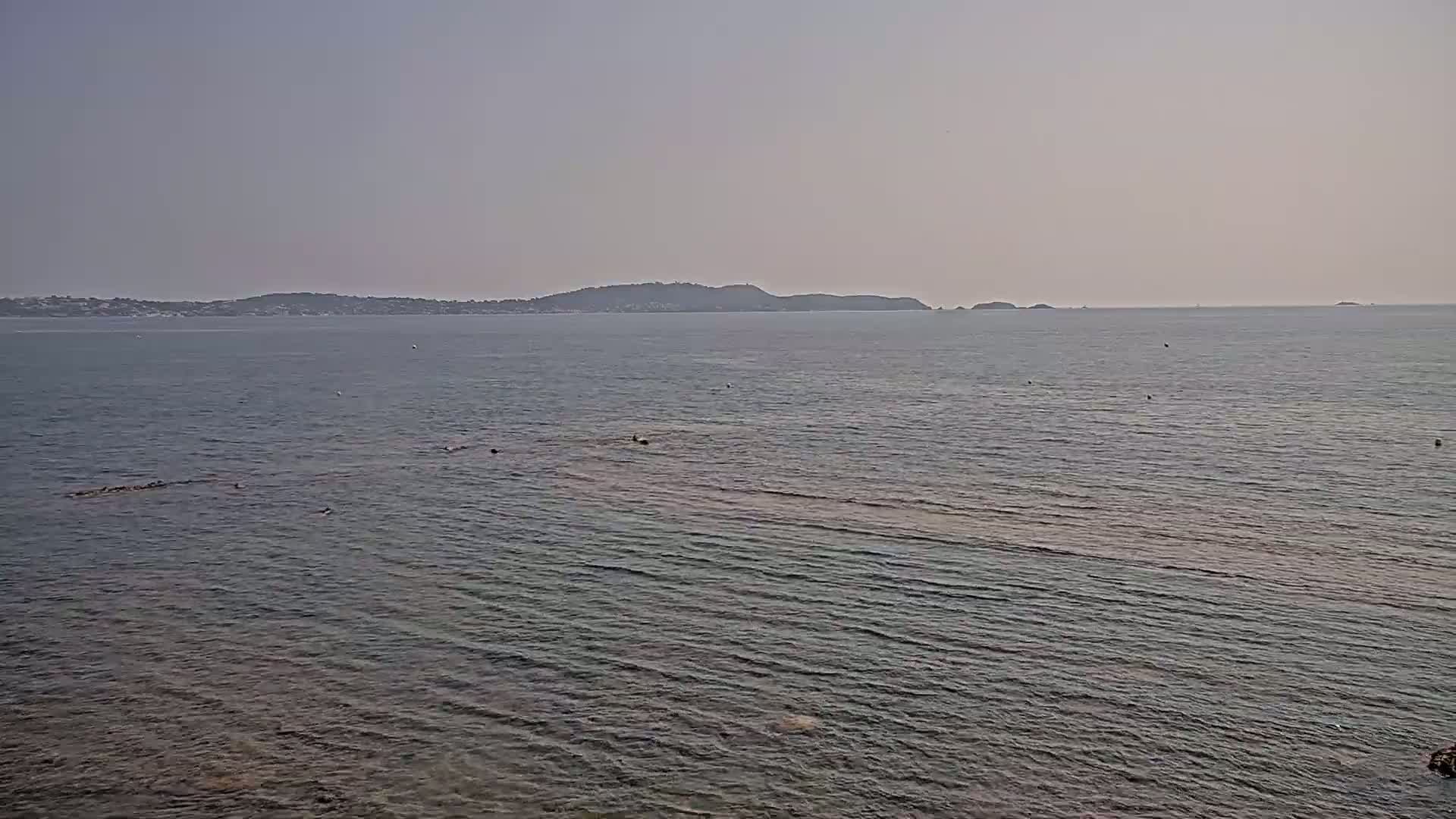 A calm, hazy sea stretches to a distant, low-lying coastline.