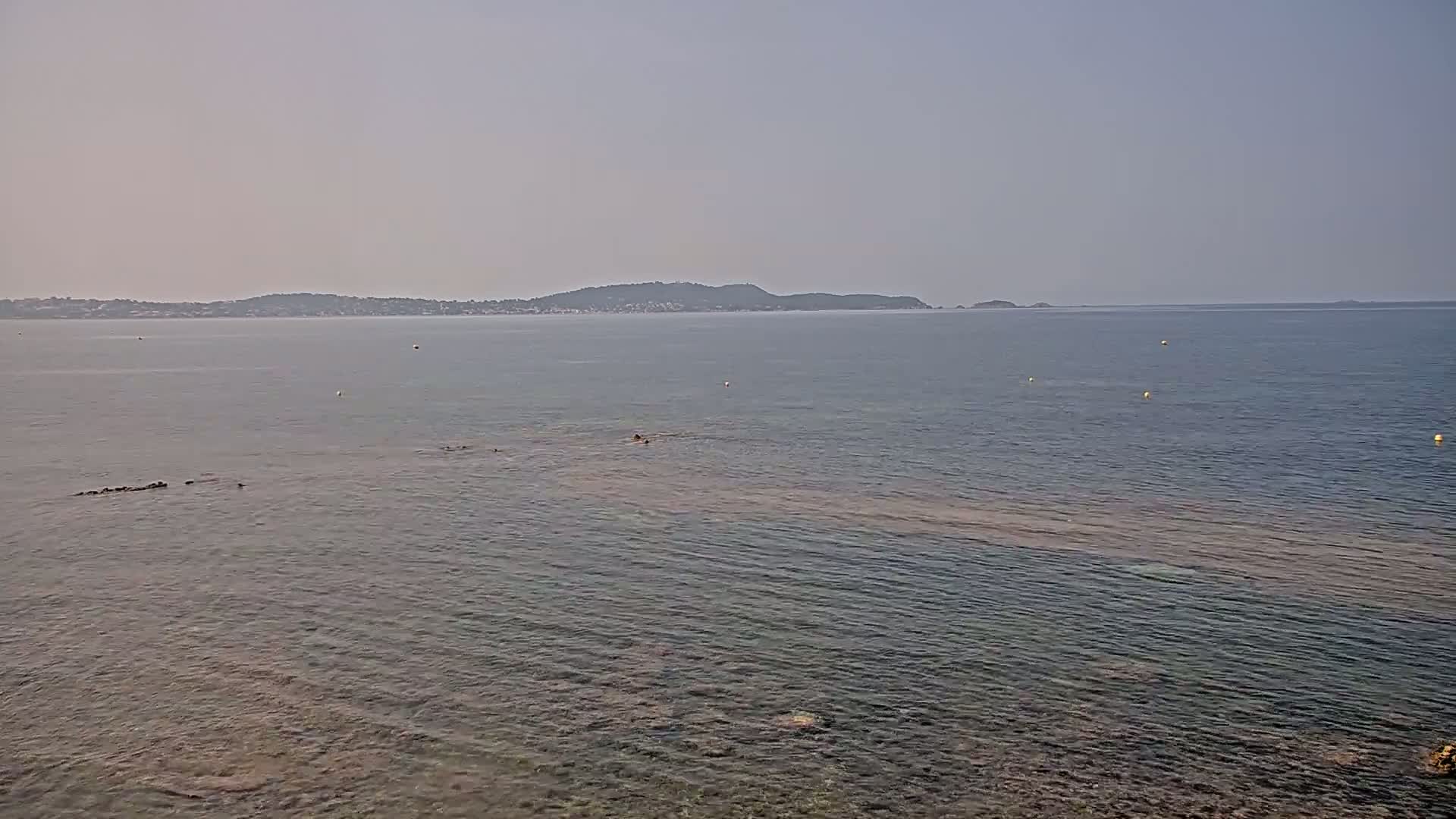 A calm, hazy sea stretches to a distant coastline with low hills under a pale sky.