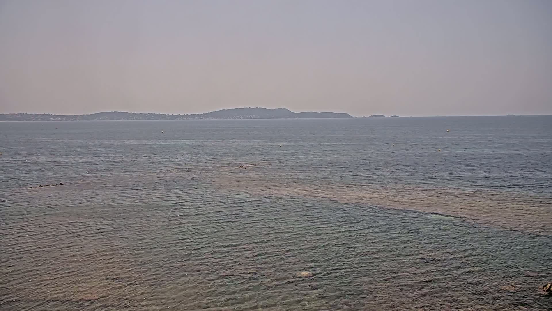 A hazy, calm sea stretches out to a distant, low-lying island.