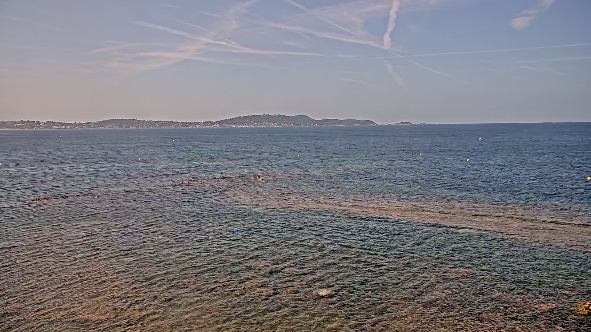 A calm sea with a distant coastline under a mostly clear sky.