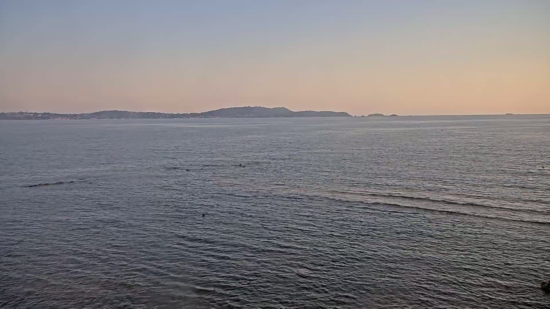 A calm ocean under a pale sunset sky shows a distant, dark mountain range on the horizon.