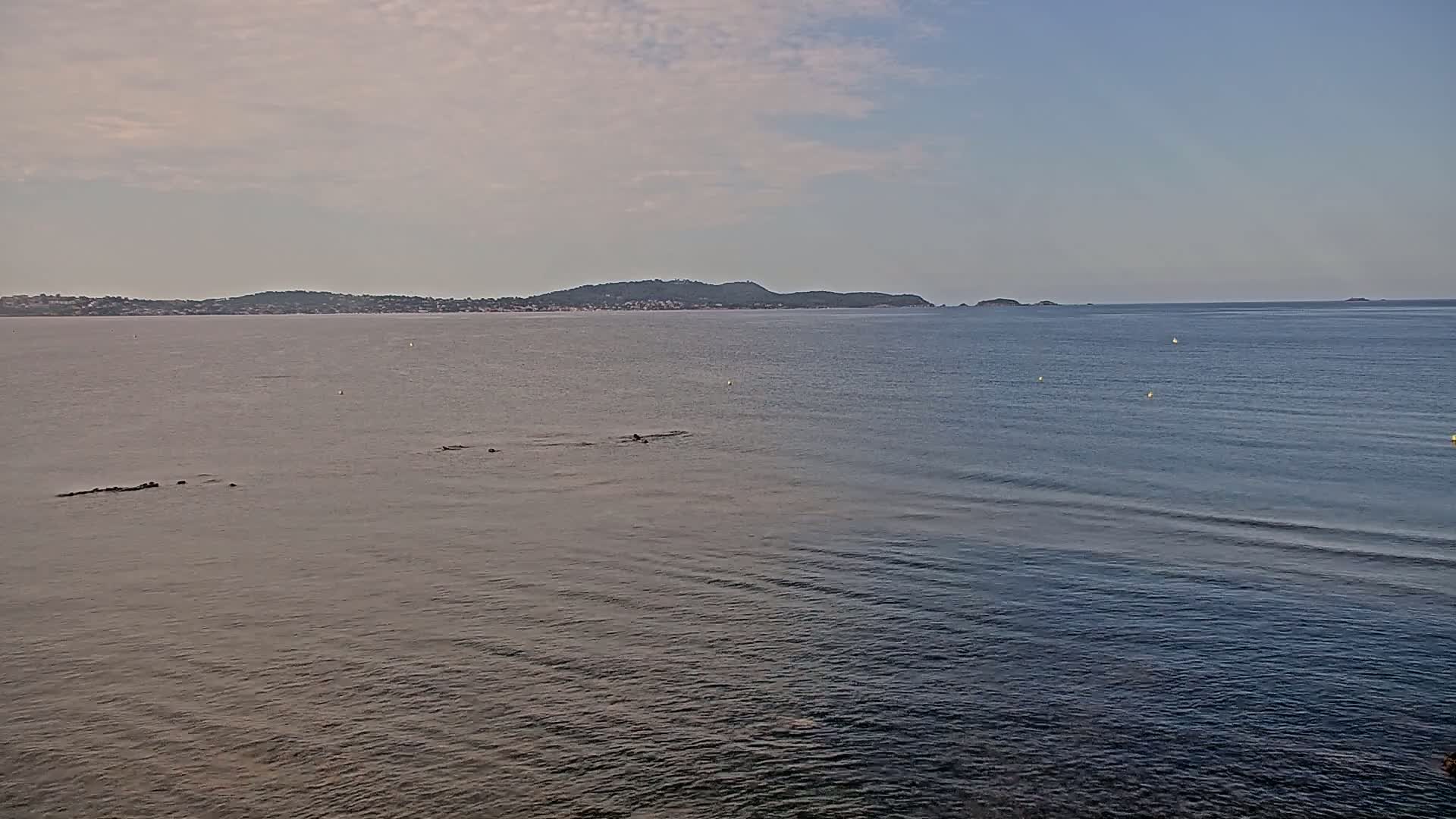 A calm sea stretches to a distant, low-lying island under a mostly cloudy sky.