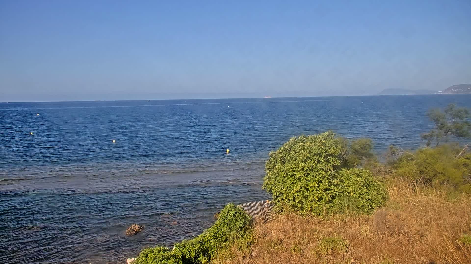 A calm, blue sea stretches to a distant shoreline under a clear sky, where scrubby vegetation grows along the coast.