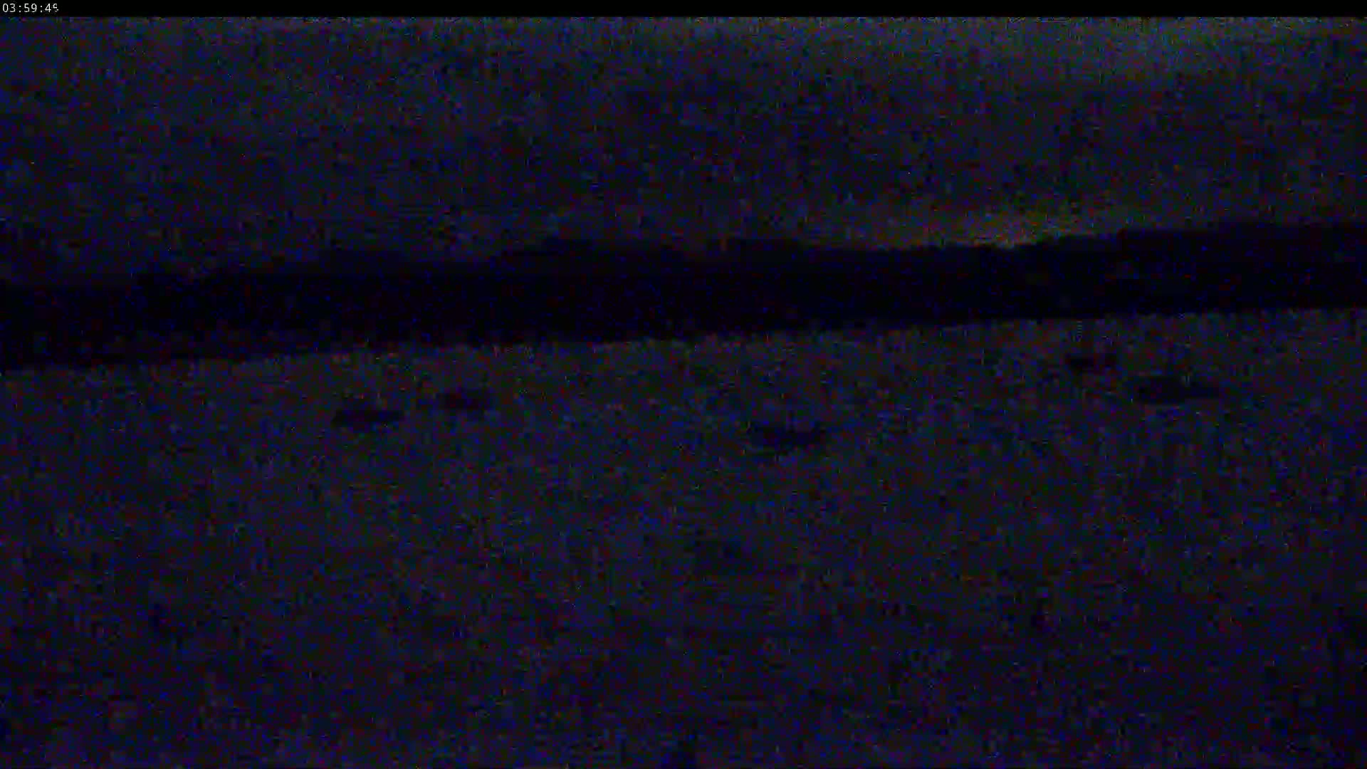 A dark, nighttime scene shows a flat expanse of land under a mostly clear, dark sky with a distant, dark horizon line.