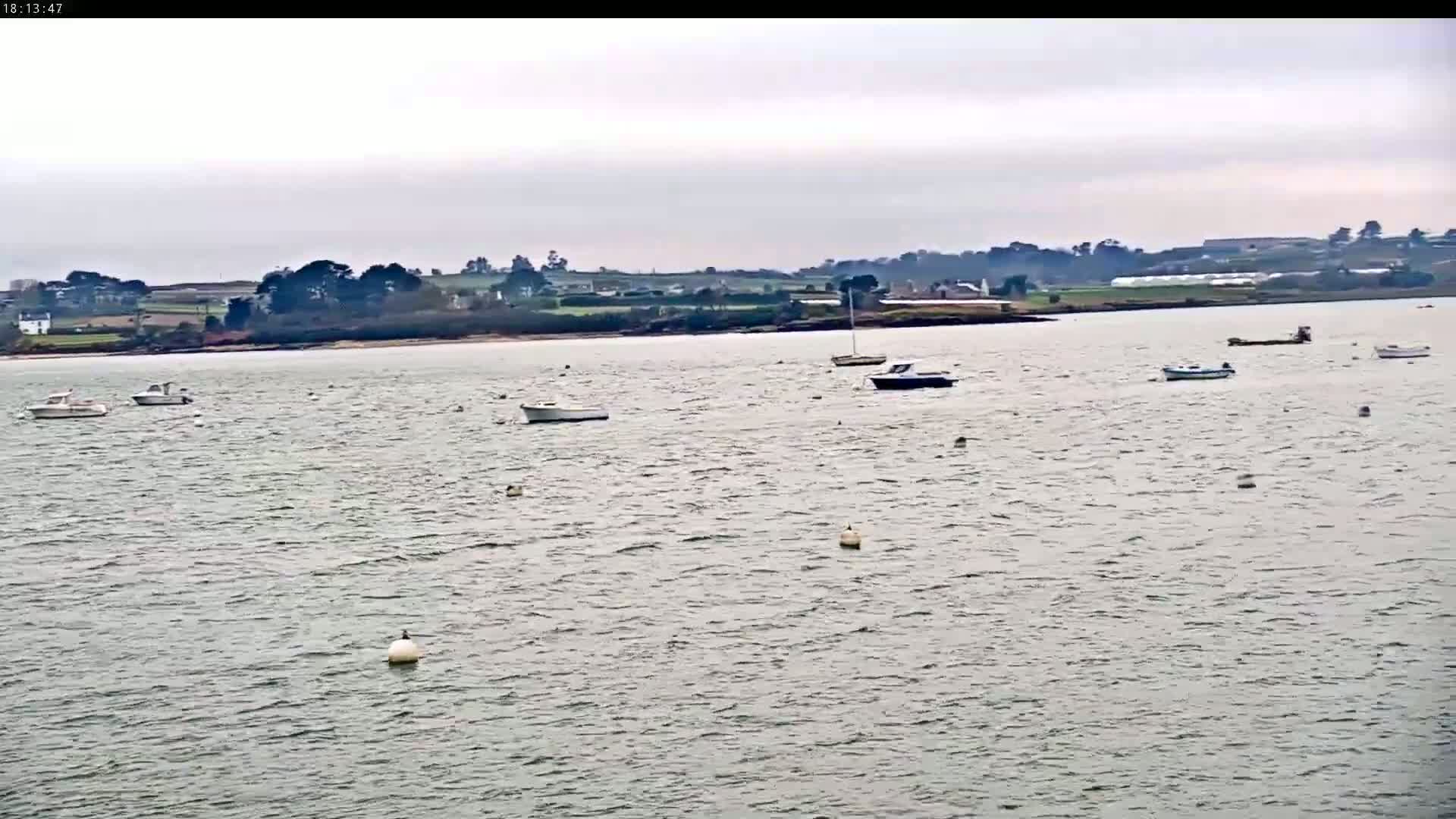 Several small boats are moored in a calm body of water under an overcast sky, with a distant shoreline visible.