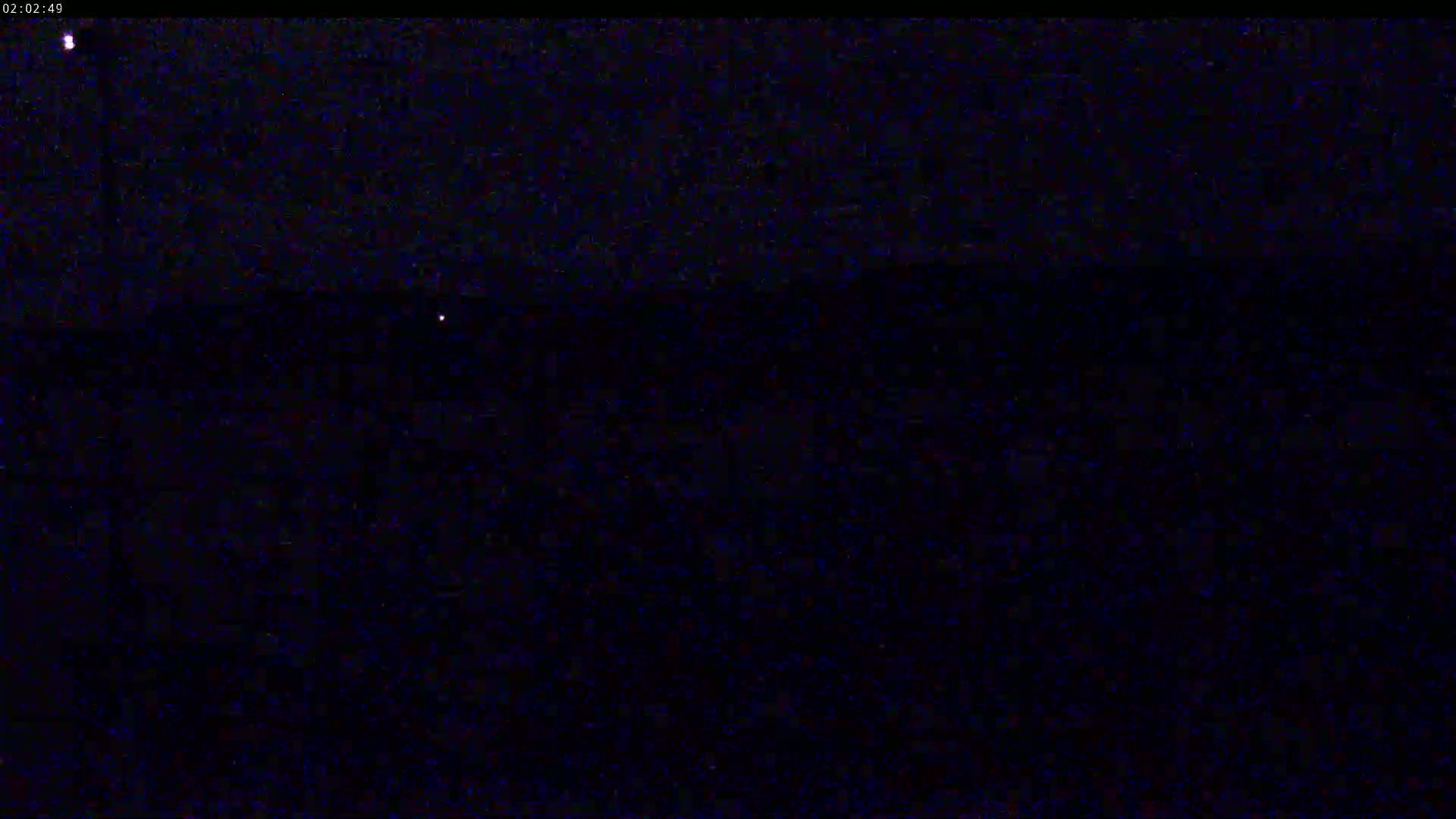 A nighttime outdoor scene shows a dark expanse with a few faint lights in the distance under a clear, dark sky.