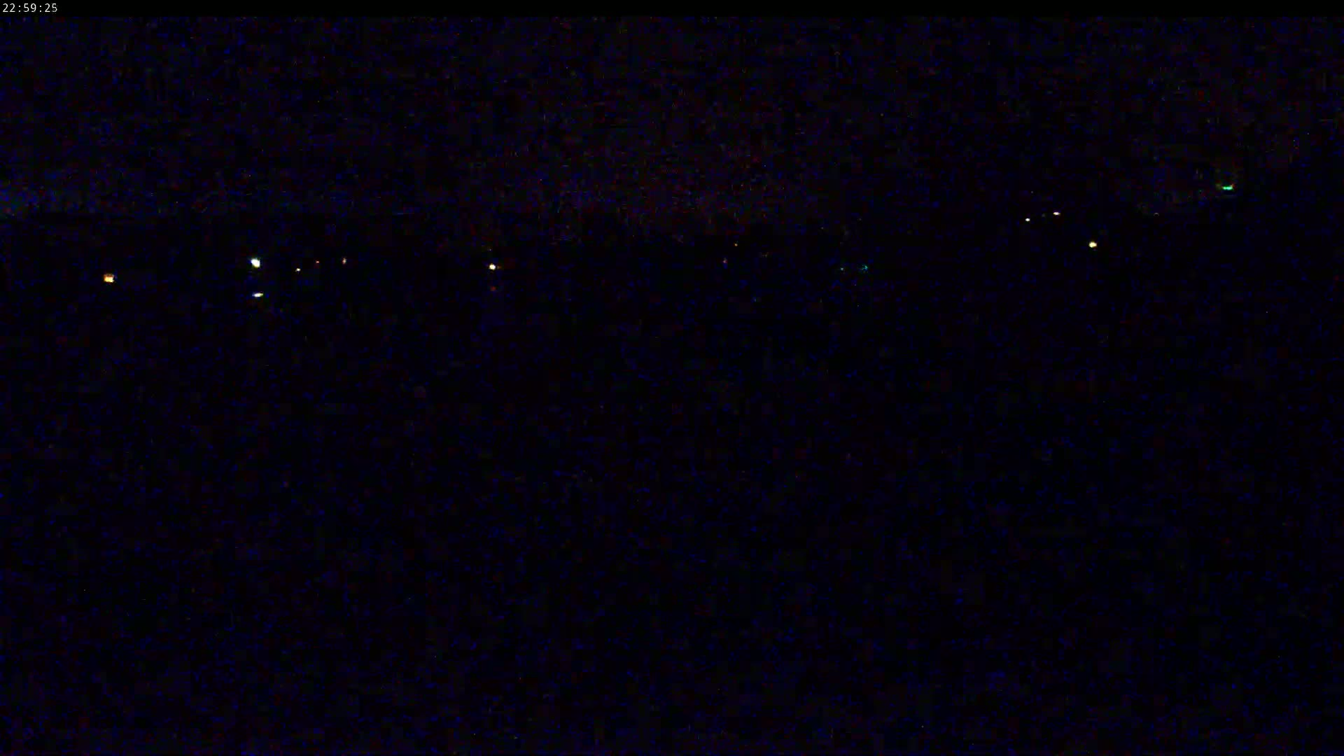 A nighttime, dark landscape is sparsely dotted with a few small, distant lights.