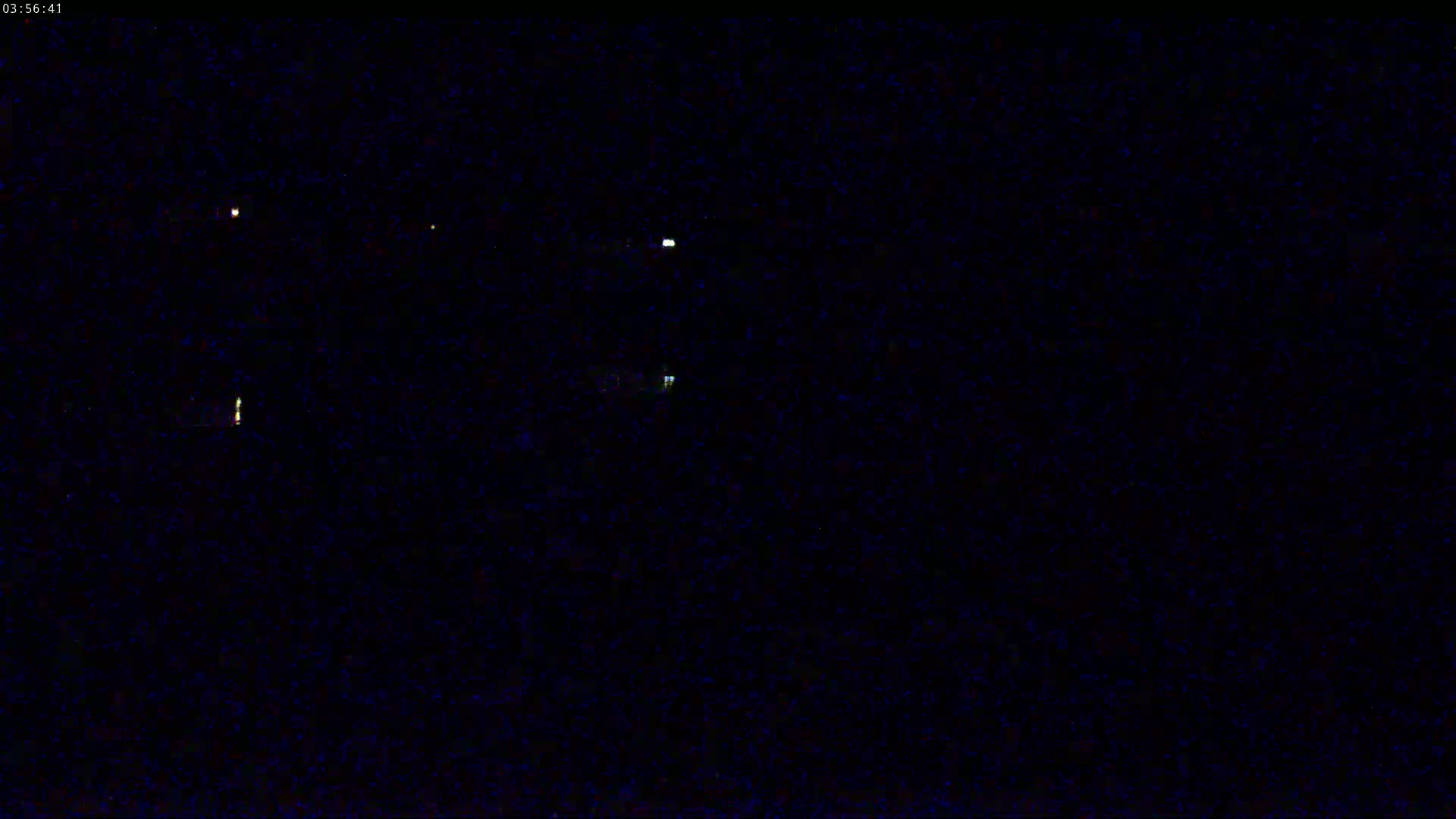 A dark, nighttime scene shows several faint, distant lights against a mostly black background.