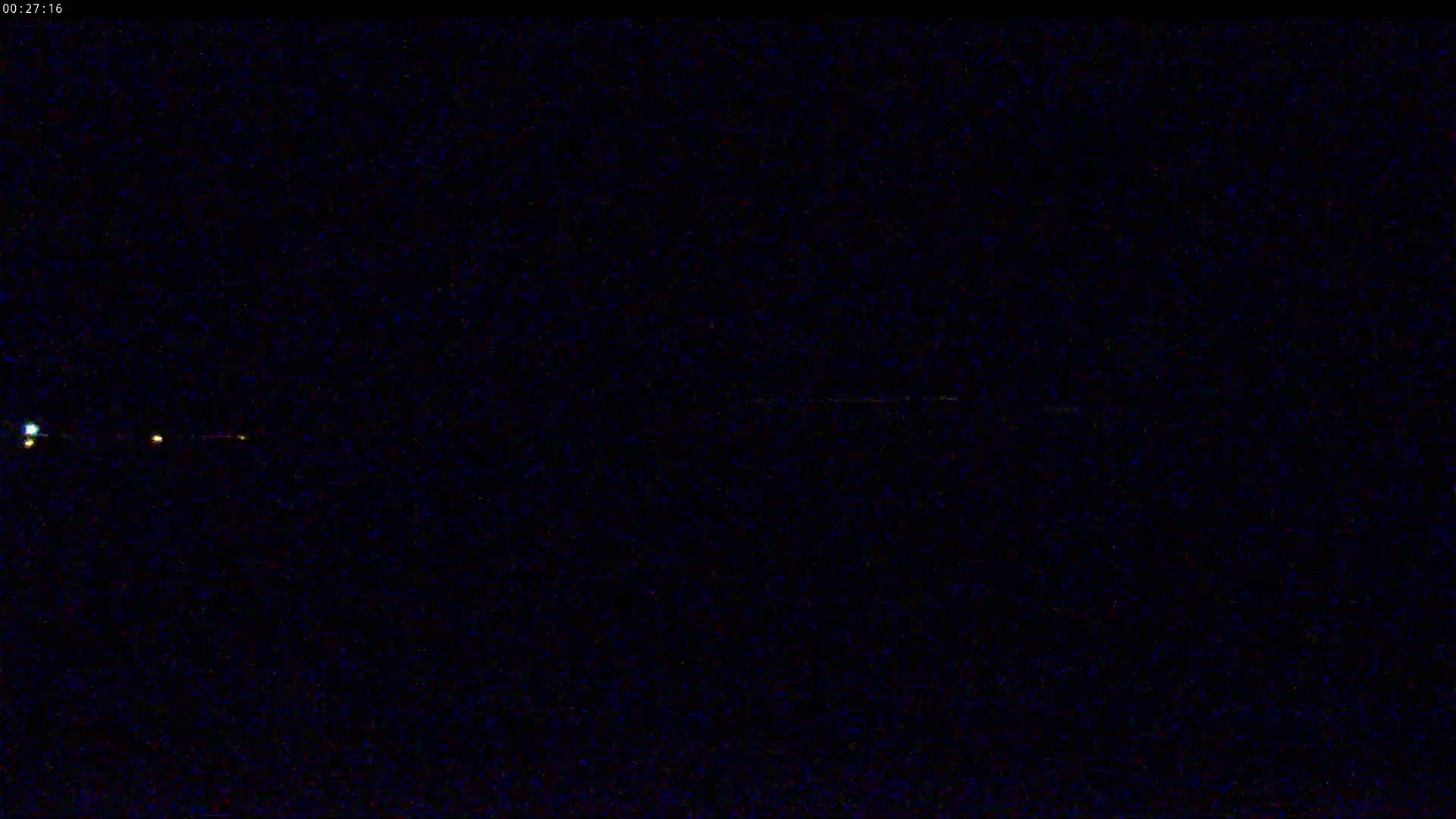 A nighttime, dark image shows a few small, faint lights in the distance.