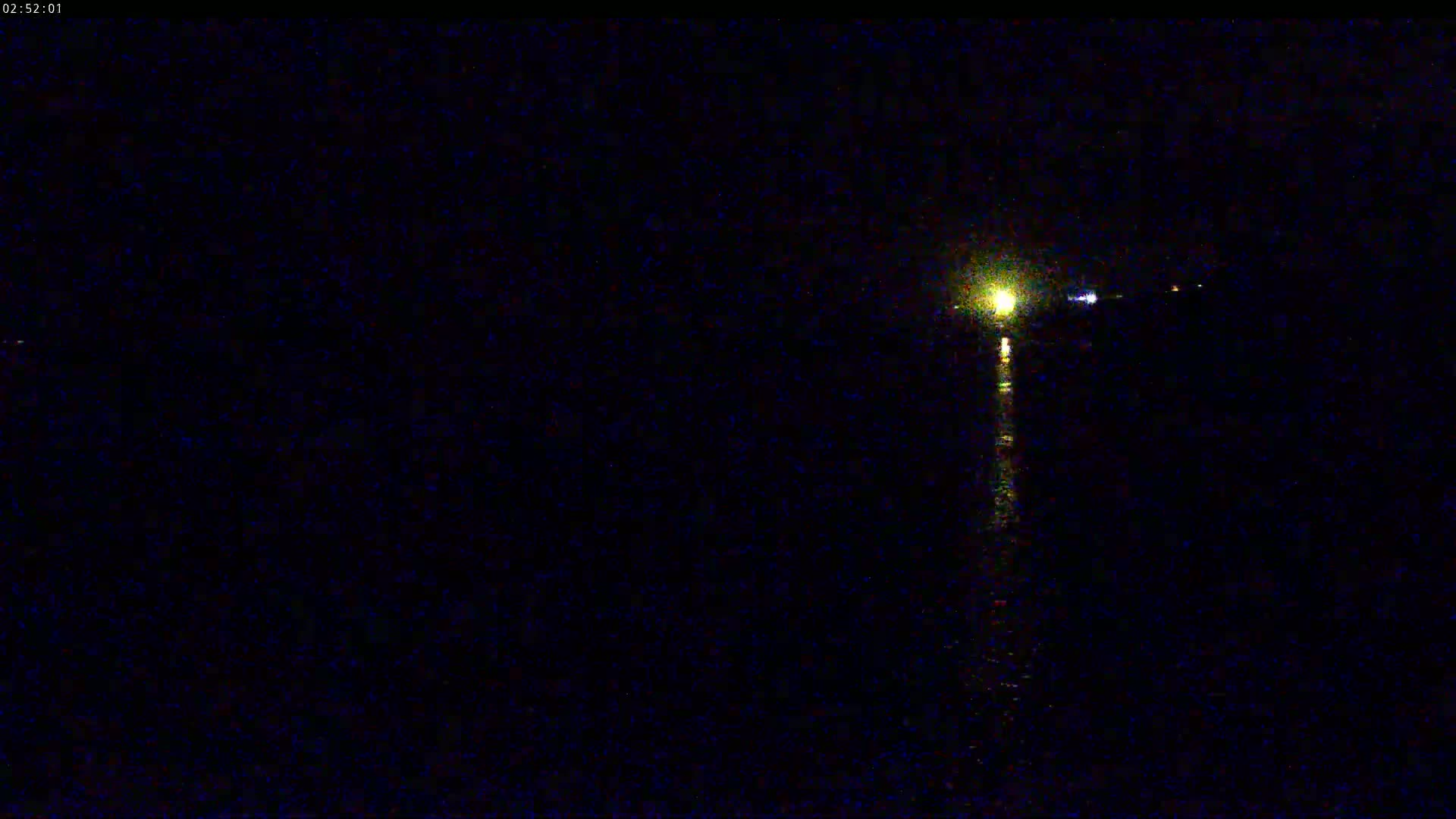 A nighttime view of a body of water shows a single light source reflecting on the dark surface.