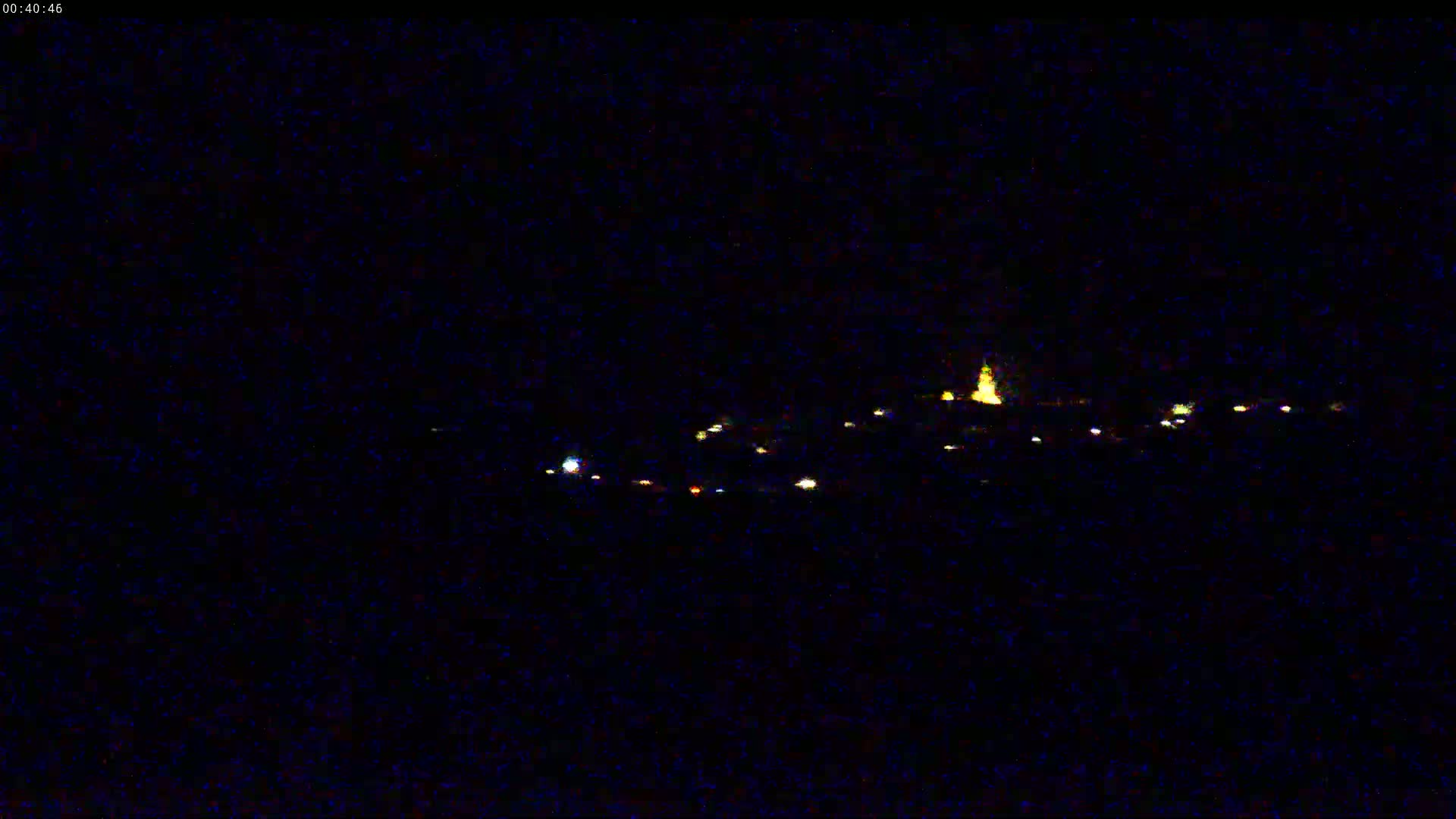 A distant collection of small, faint lights, possibly a small town, is visible at night under a dark, clear sky.