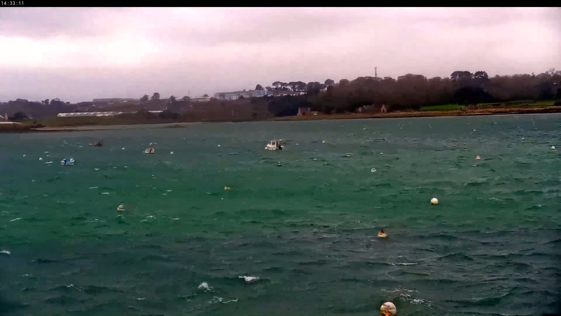 A choppy, dark-green body of water dotted with small boats and buoys under an overcast sky.