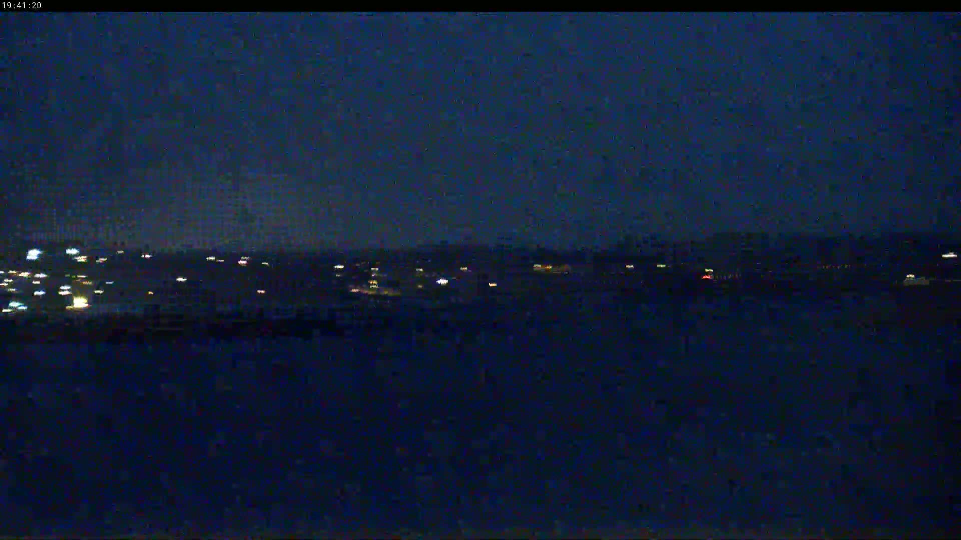 A dark, nighttime view shows a distant line of lights from a town or city, under a clear, dark sky.