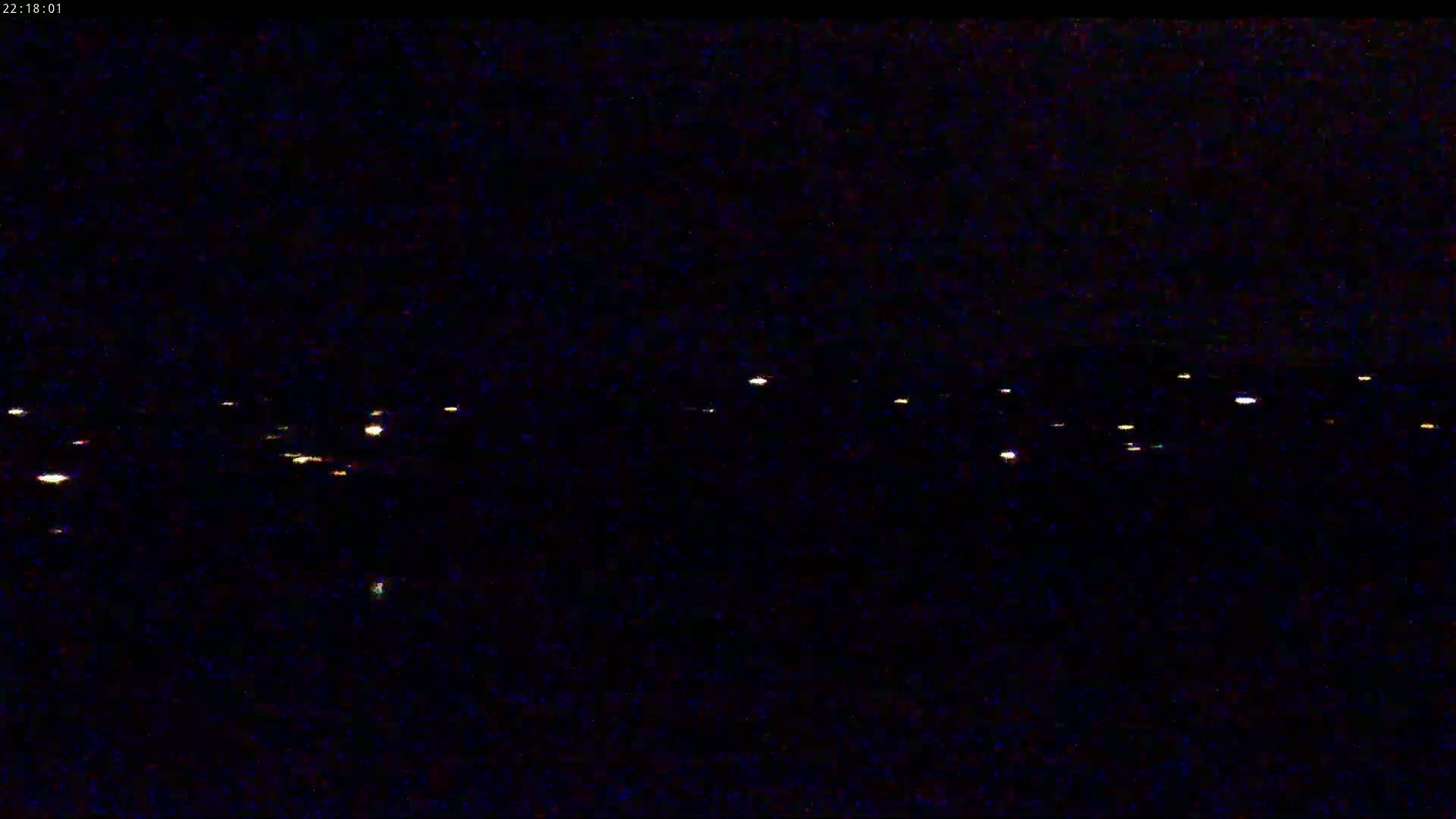 A nighttime long shot shows a line of faint, distant lights across a dark, possibly water, surface.