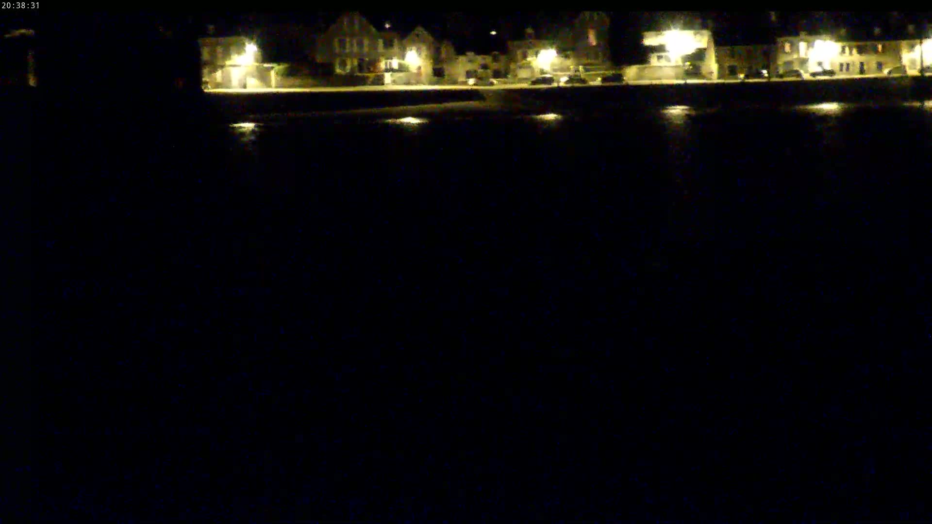 A nighttime view of a row of lit buildings reflected in dark water under a clear, dark sky.