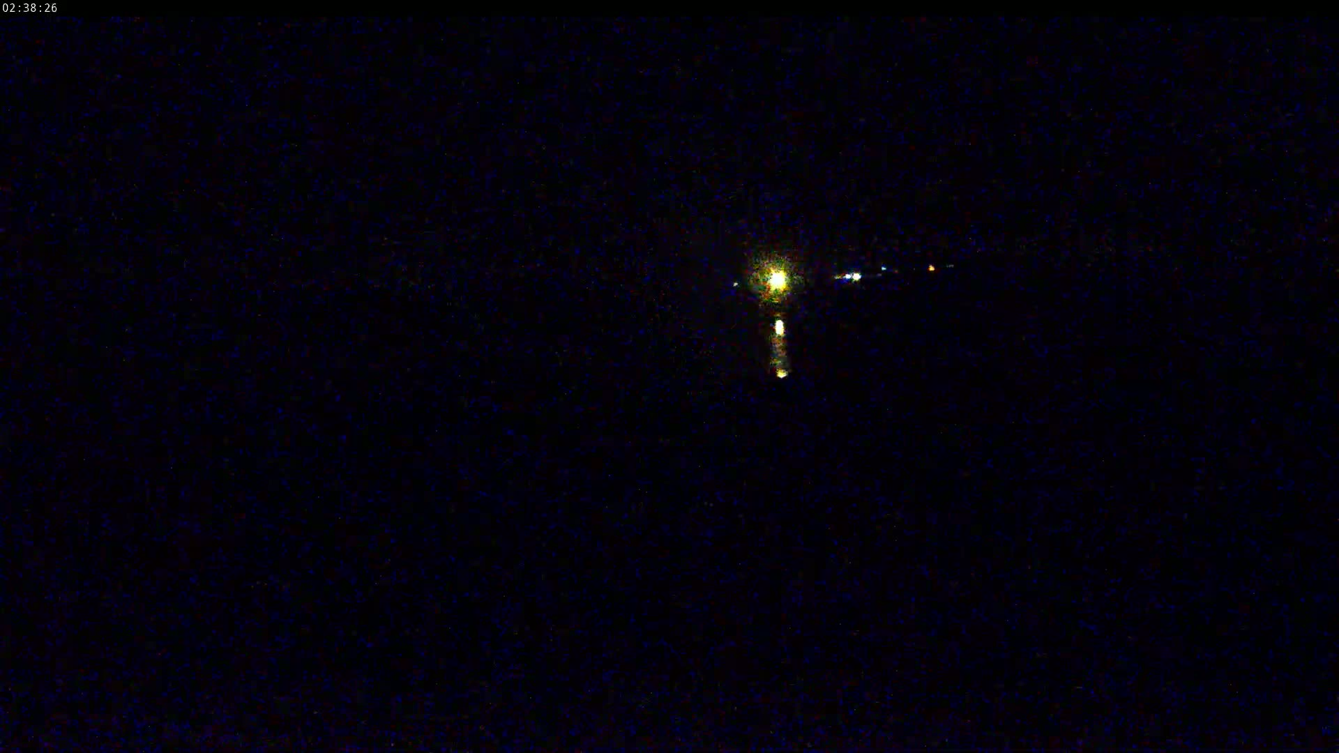 A nighttime image shows a distant light source reflecting on a dark body of water.
