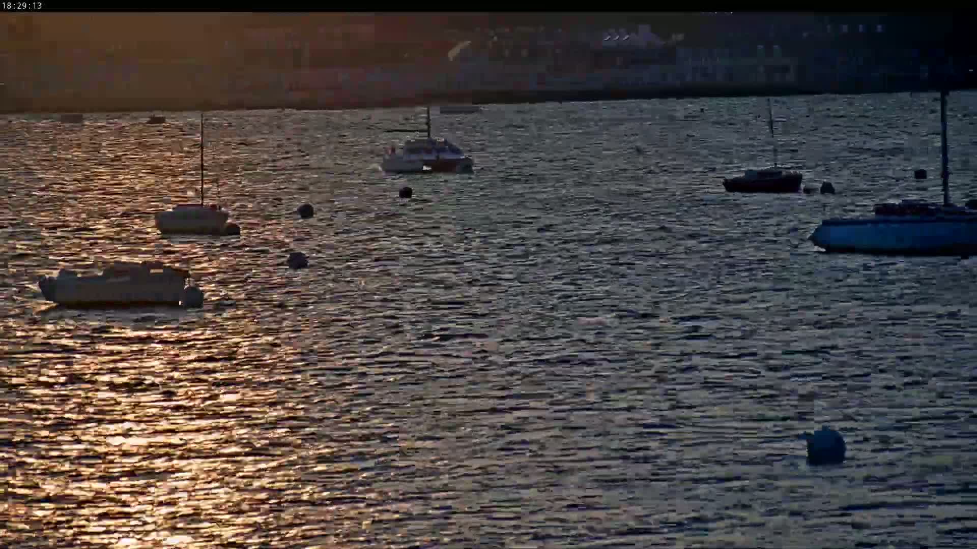 Several small boats are moored in calm water at sunset, with a distant shoreline visible in the background.