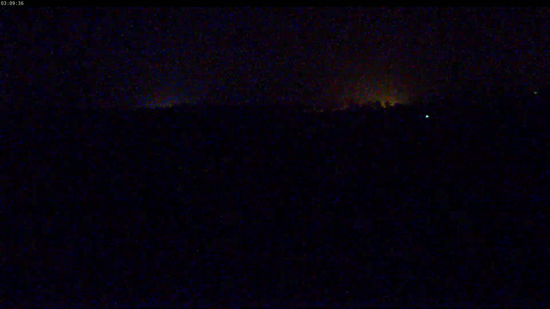 A dark, nighttime scene shows a distant line of faint, orange lights against a black sky.