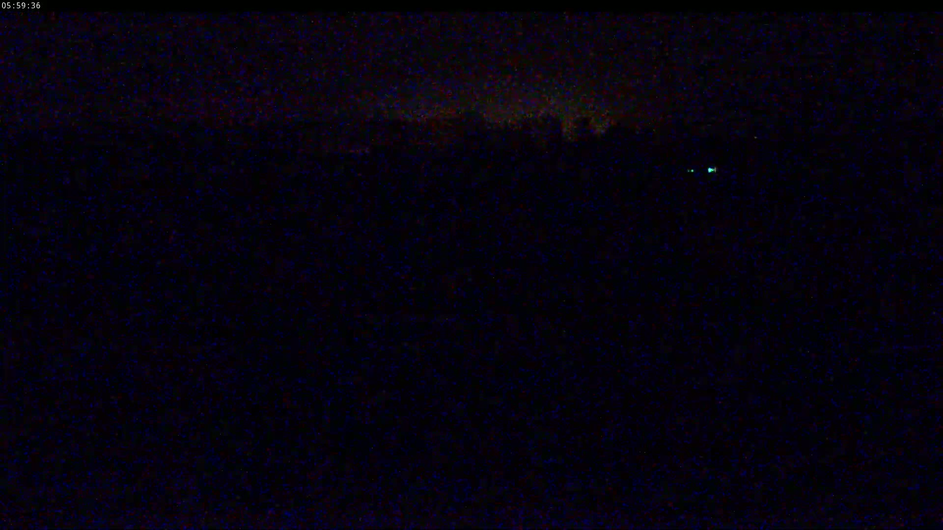 A nighttime, dark, outdoor scene shows a blurry, indistinct landscape under a mostly clear sky.
