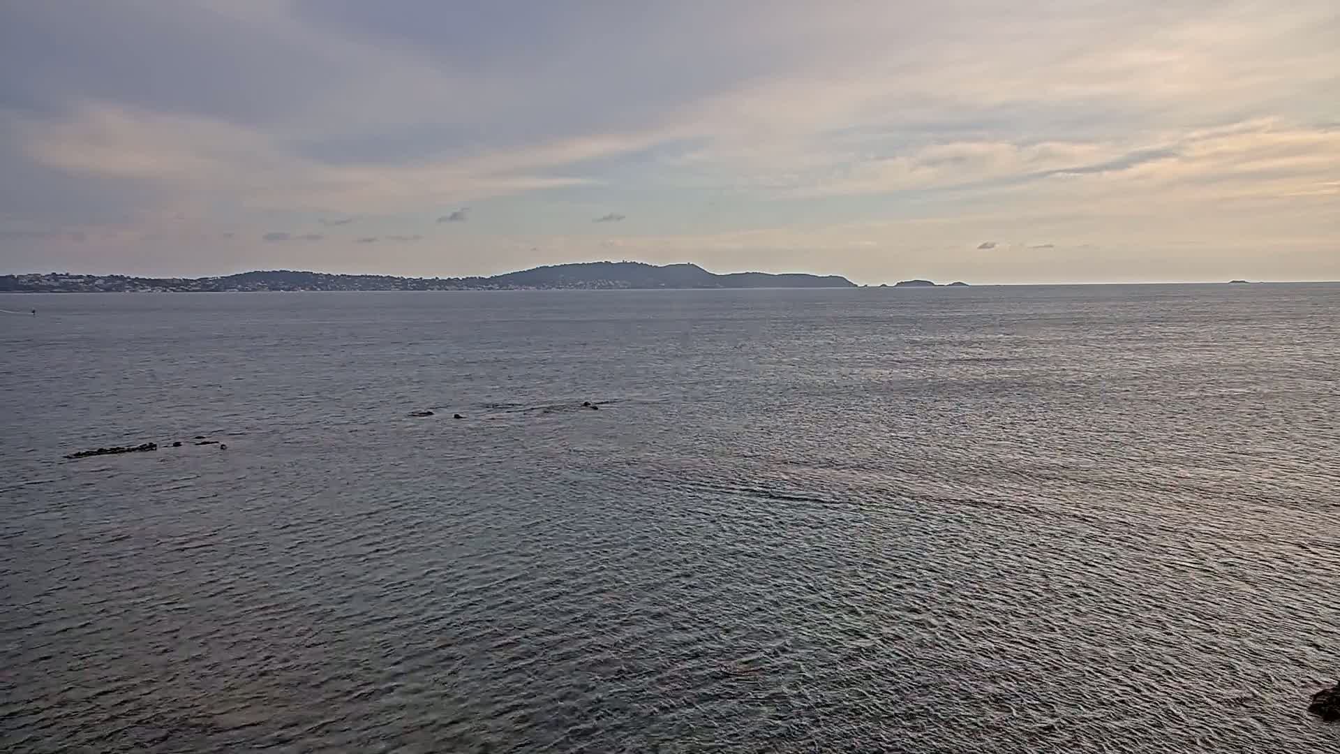A calm, gray-blue sea stretches to a distant shoreline under a cloudy, pale sky.