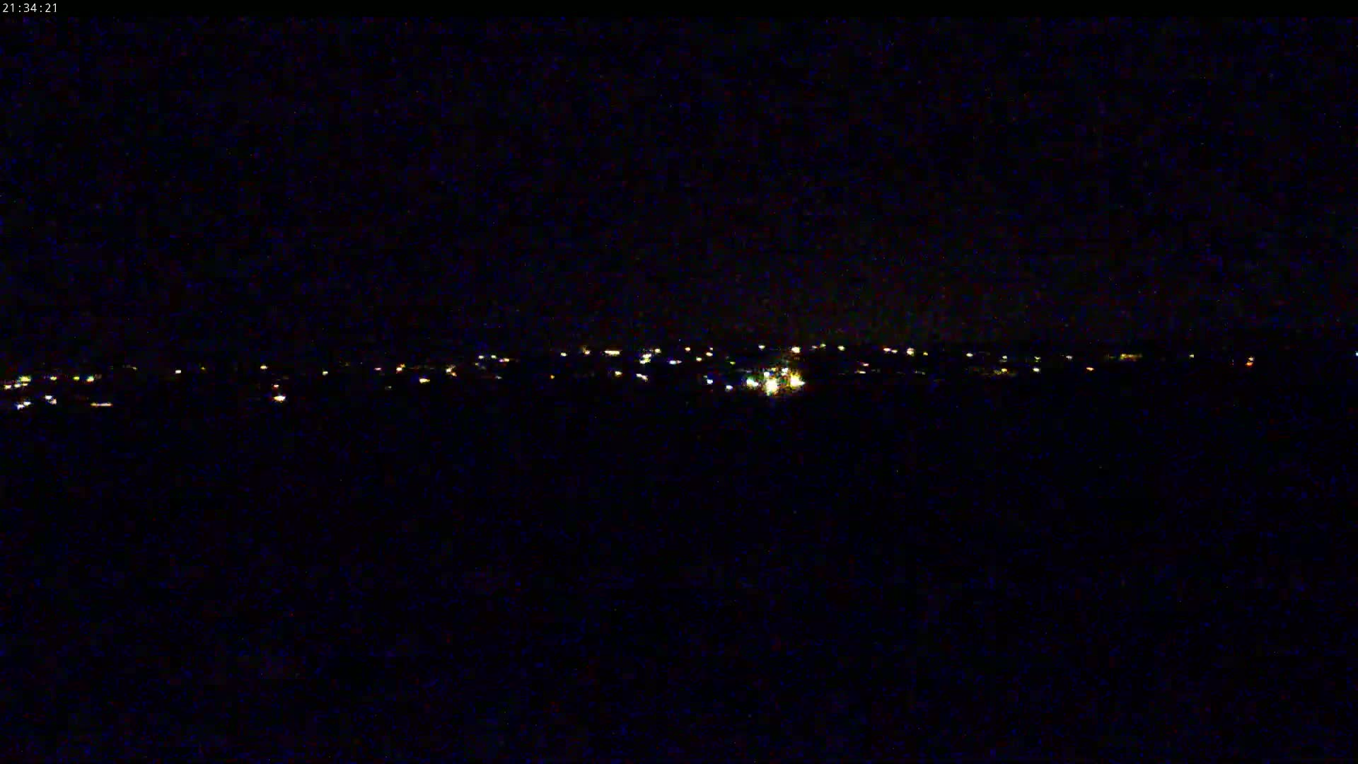 A nighttime long shot shows a distant line of faint, scattered lights on a dark horizon under a clear, black sky.