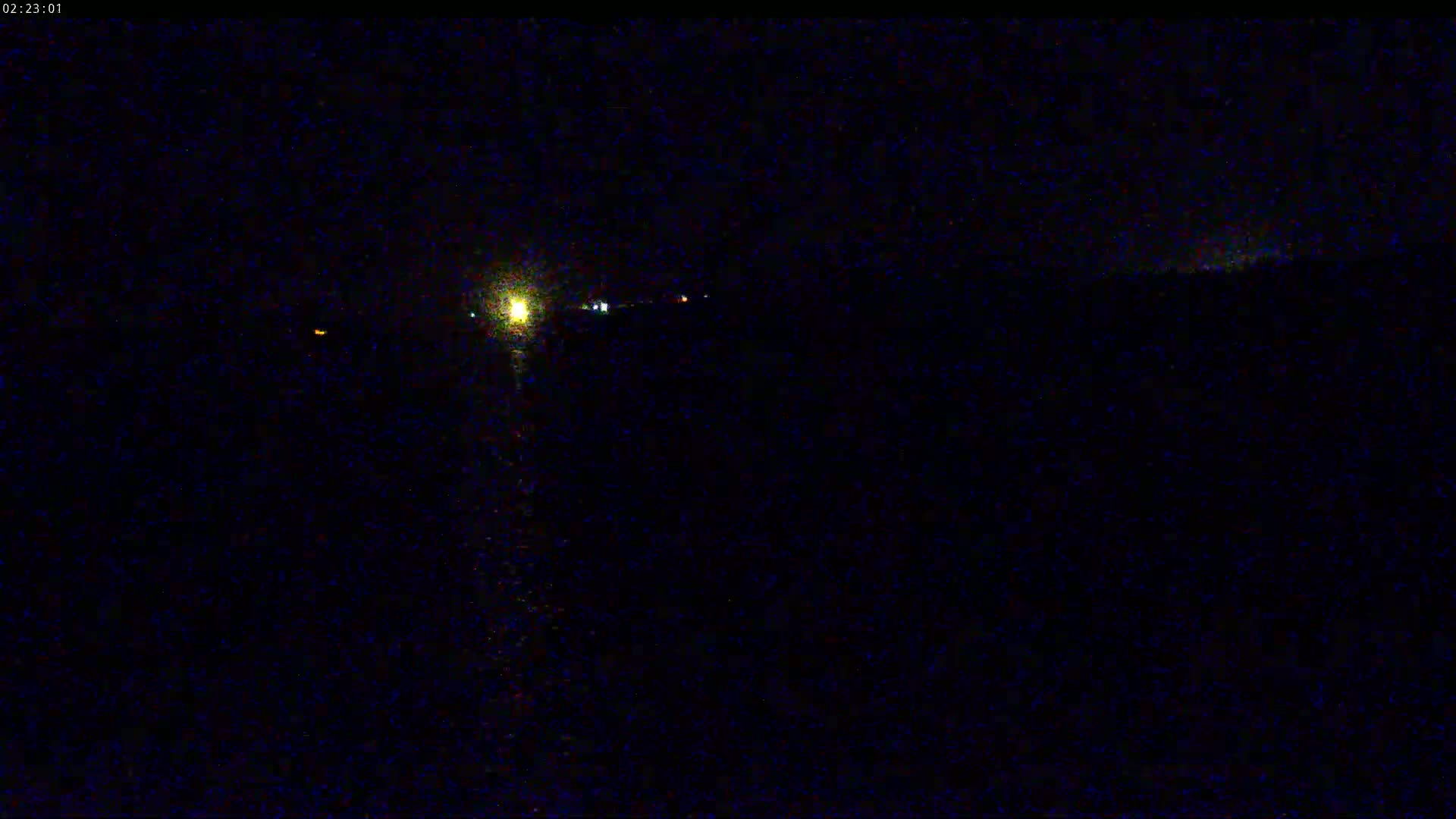 A nighttime, low-light view shows a dark landscape with a few faint lights in the distance.
