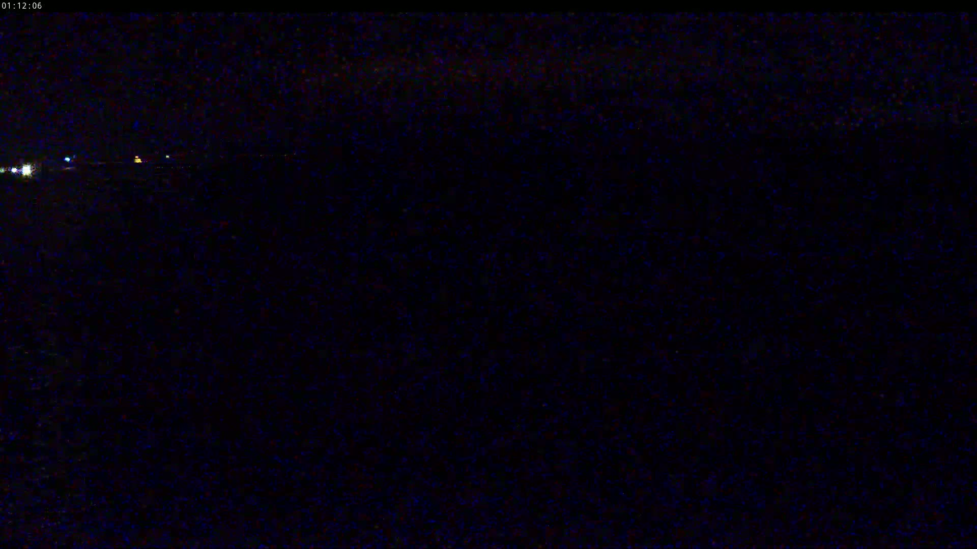 A nighttime, low-light image shows a dark landscape with a few faint lights in the distance.