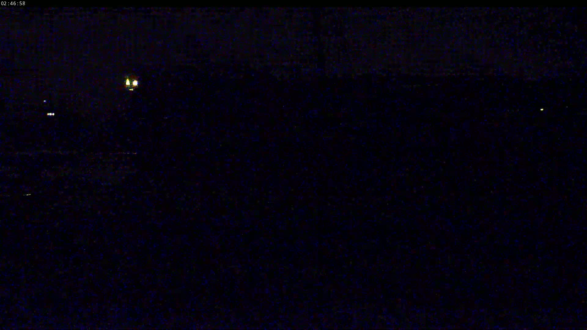 A dark, nighttime scene shows a few faint lights in the distance.