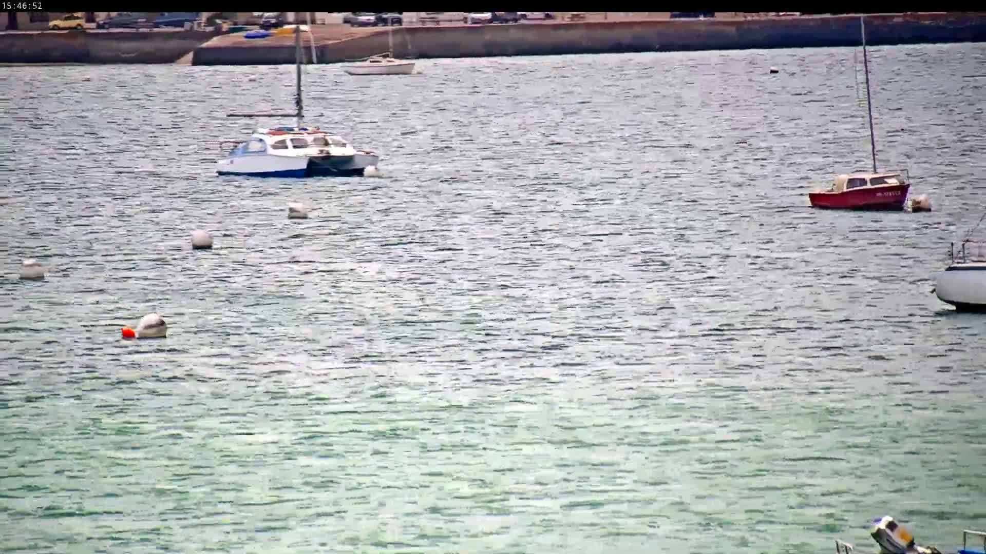 Several small boats are moored in calm, light-green water near a stone embankment.