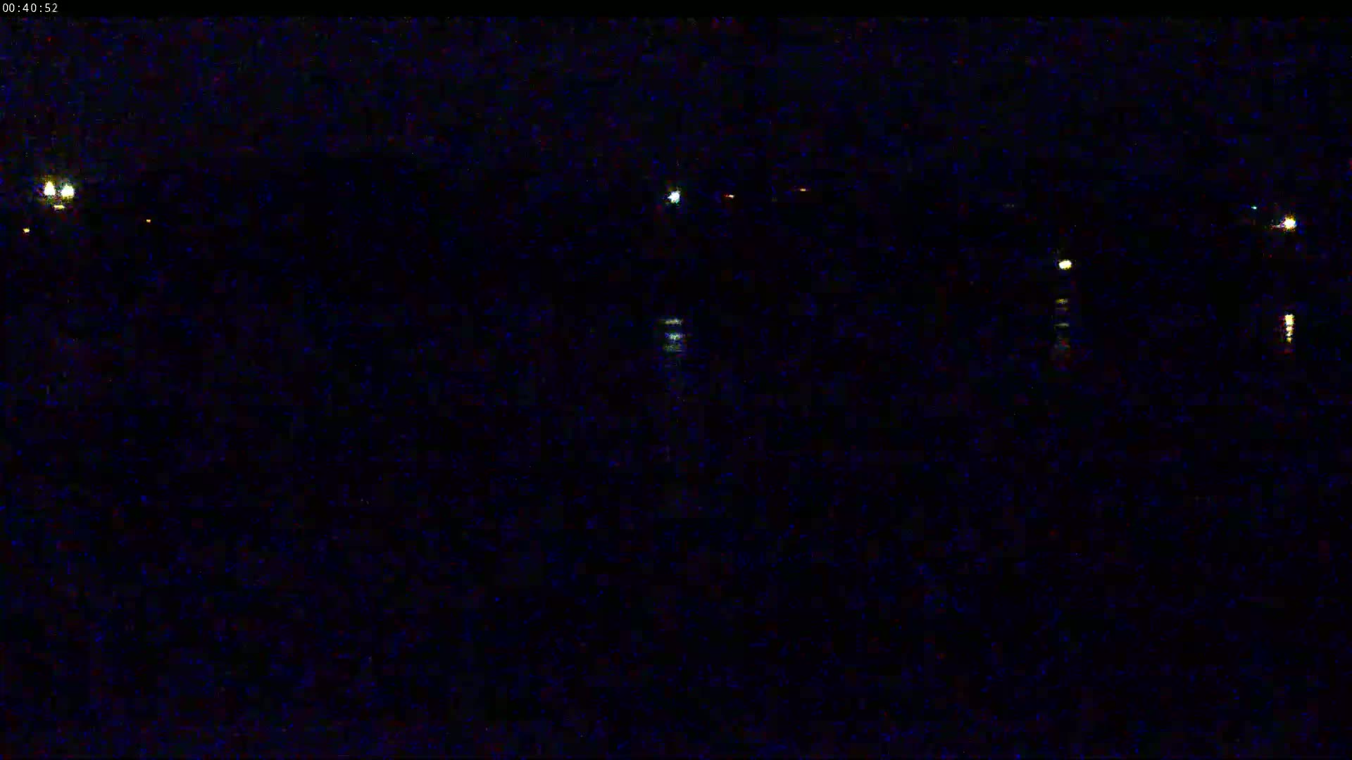 At night, a dark body of water reflects a few distant lights.