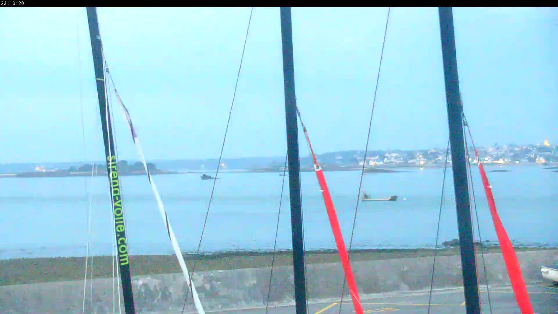 Several sailboat masts and rigging are in the foreground, overlooking a calm body of water with a distant shoreline under a twilight sky.