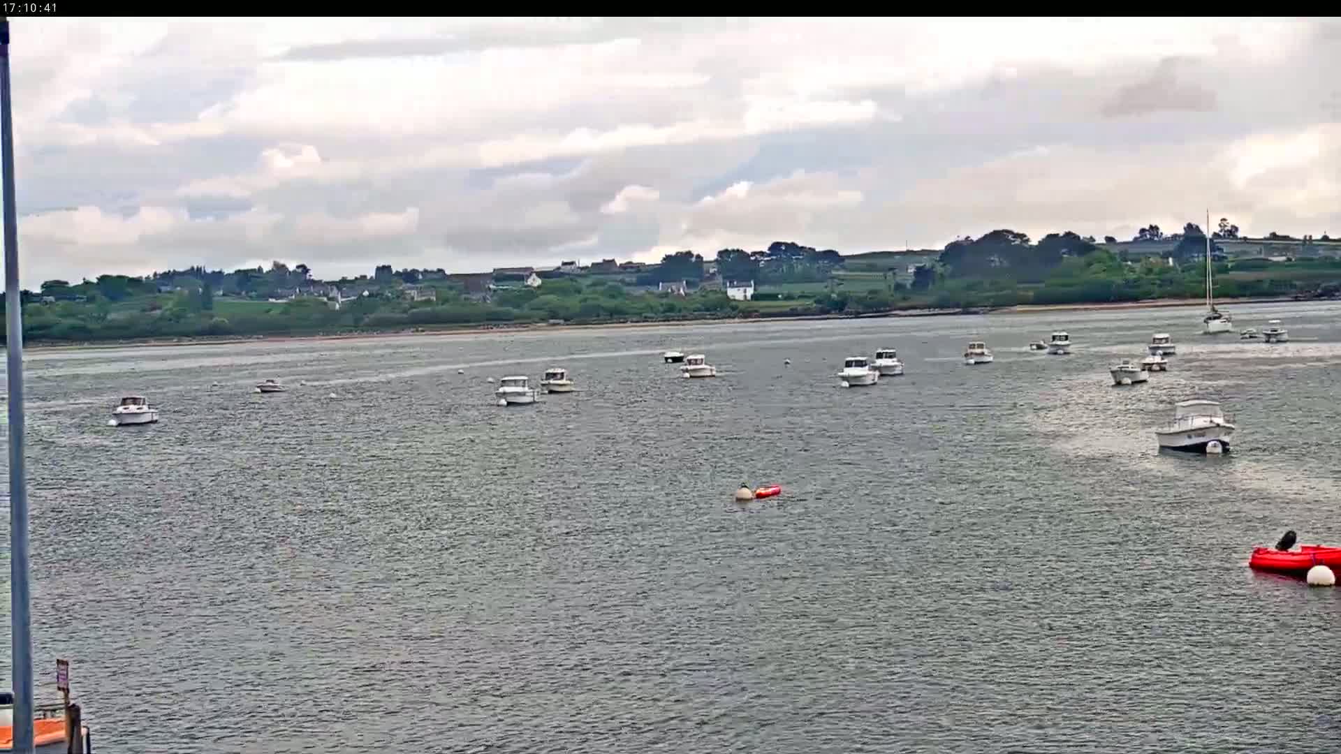 Numerous small white motorboats are moored in calm, grey water under a partly cloudy sky, with a distant shoreline visible.