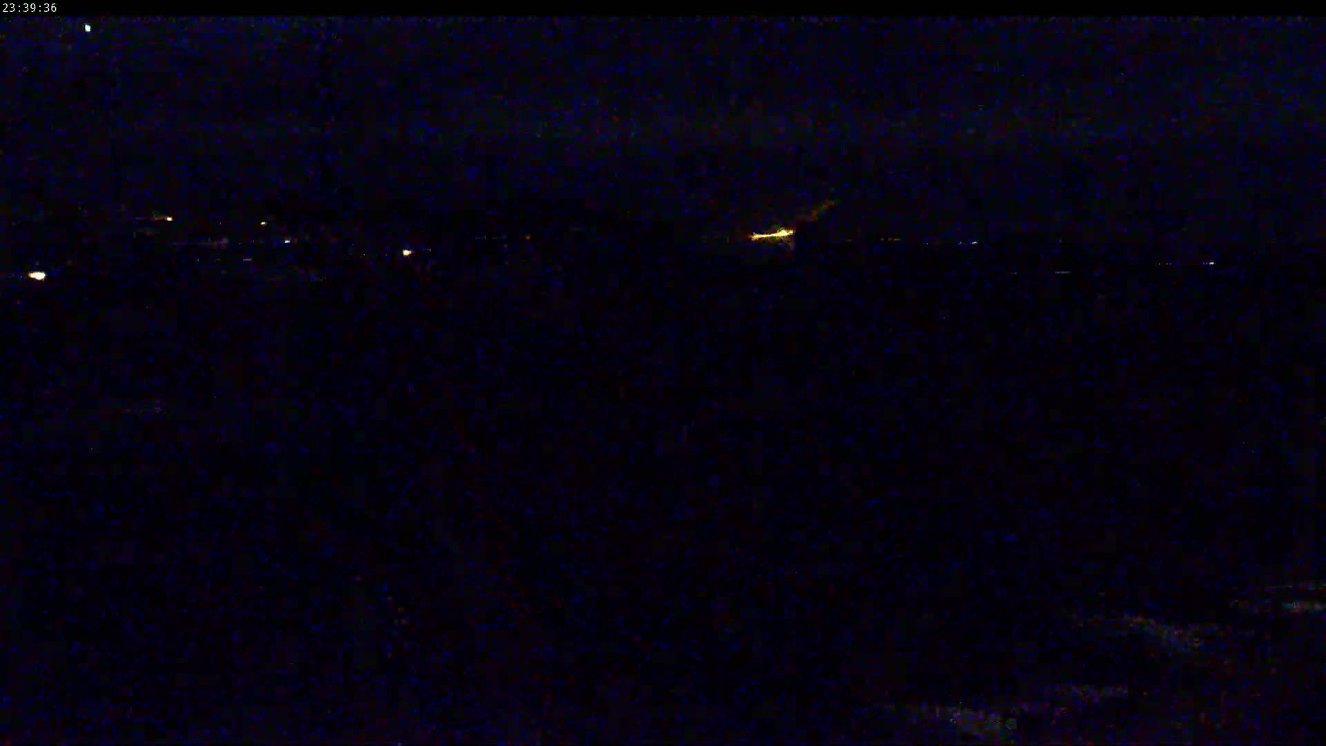 A nighttime long shot shows a dark landscape with a few distant lights and a bright, blurry light source in the center.