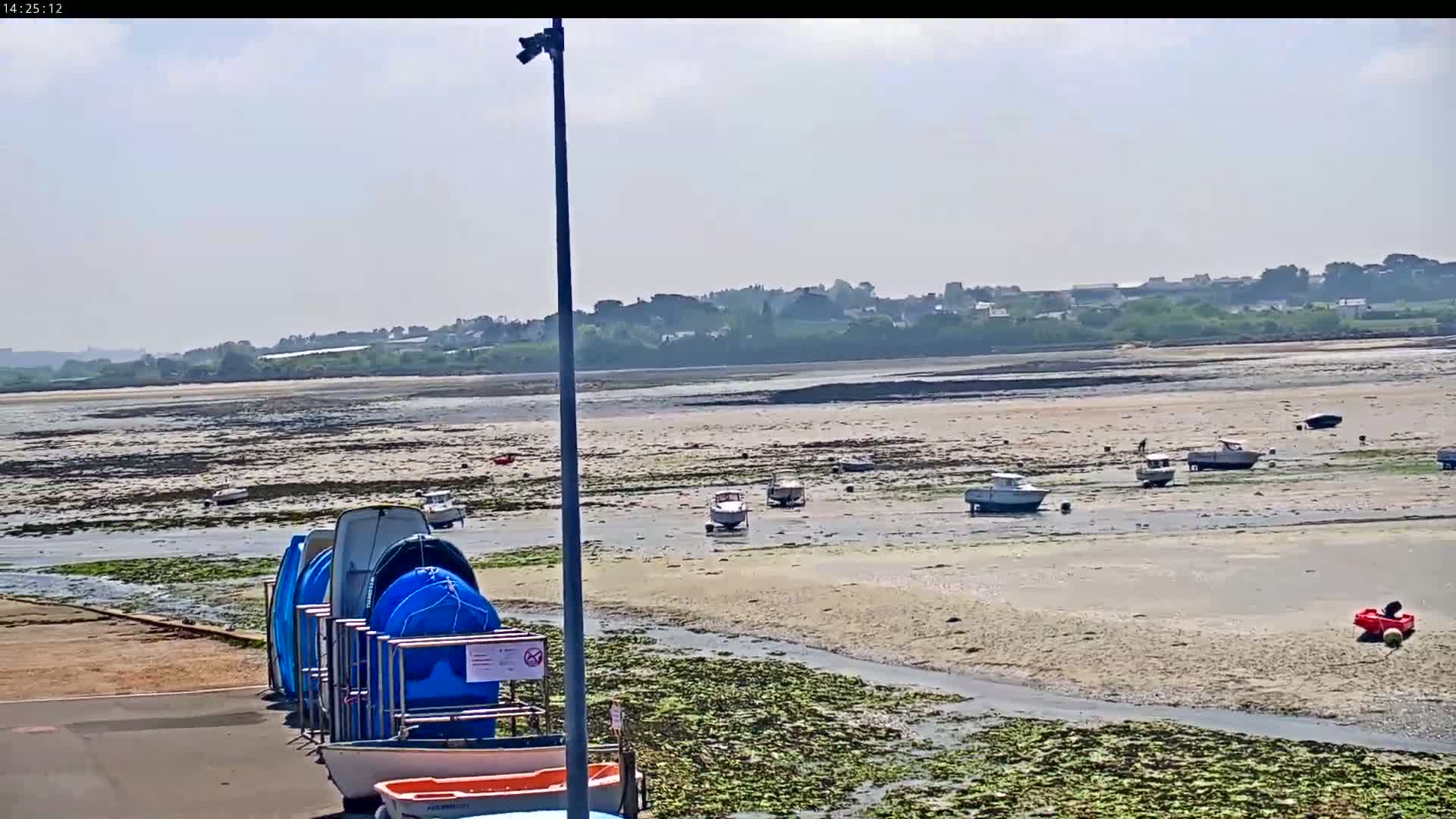 A sandy shoreline at low tide, dotted with small boats, is visible beneath a mostly clear sky, with several boats stored upright on a rack in the foreground.