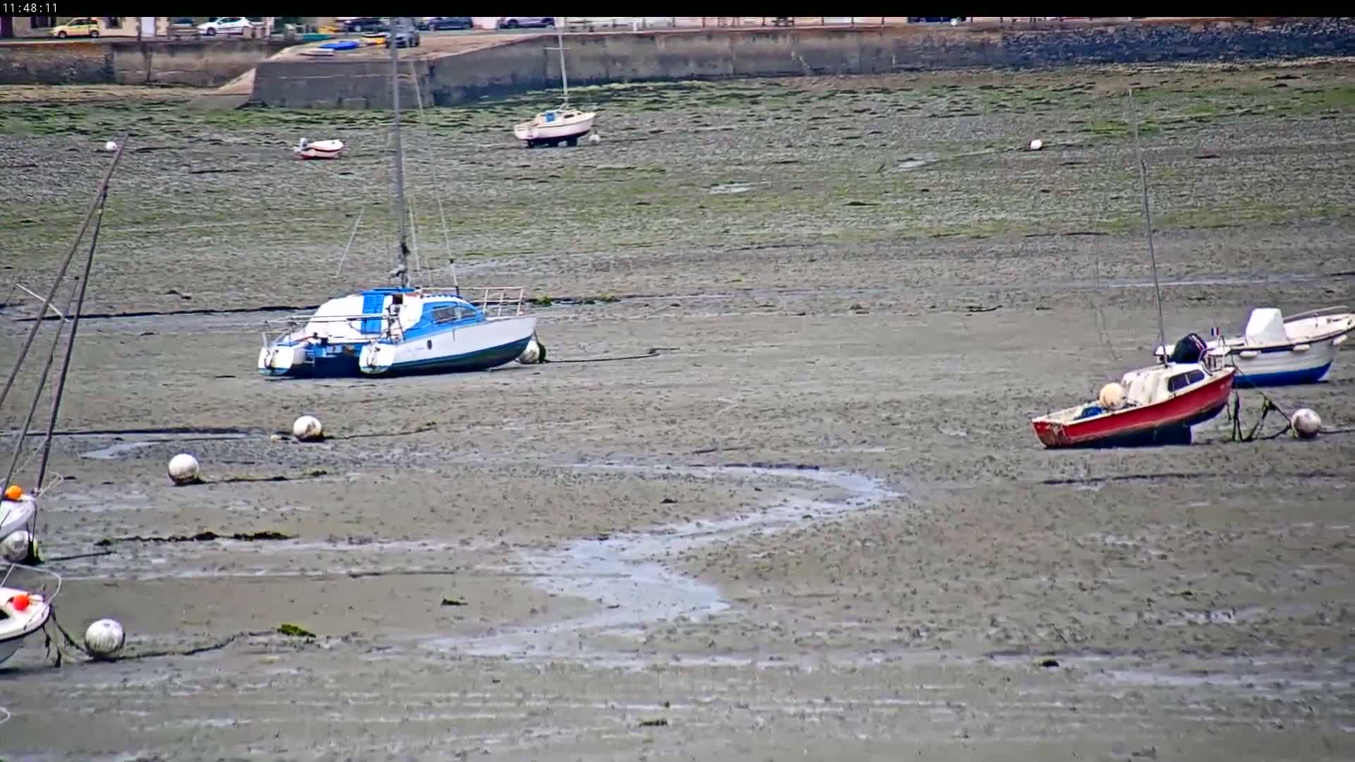 Several boats are grounded on a muddy, low-tide shoreline.
